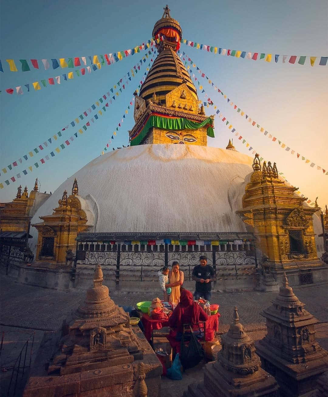 桌布 壁紙 — 金色佛塔，白色圓頂和經幡沐浴在溫暖的夕陽光中，人們聚集在下方。