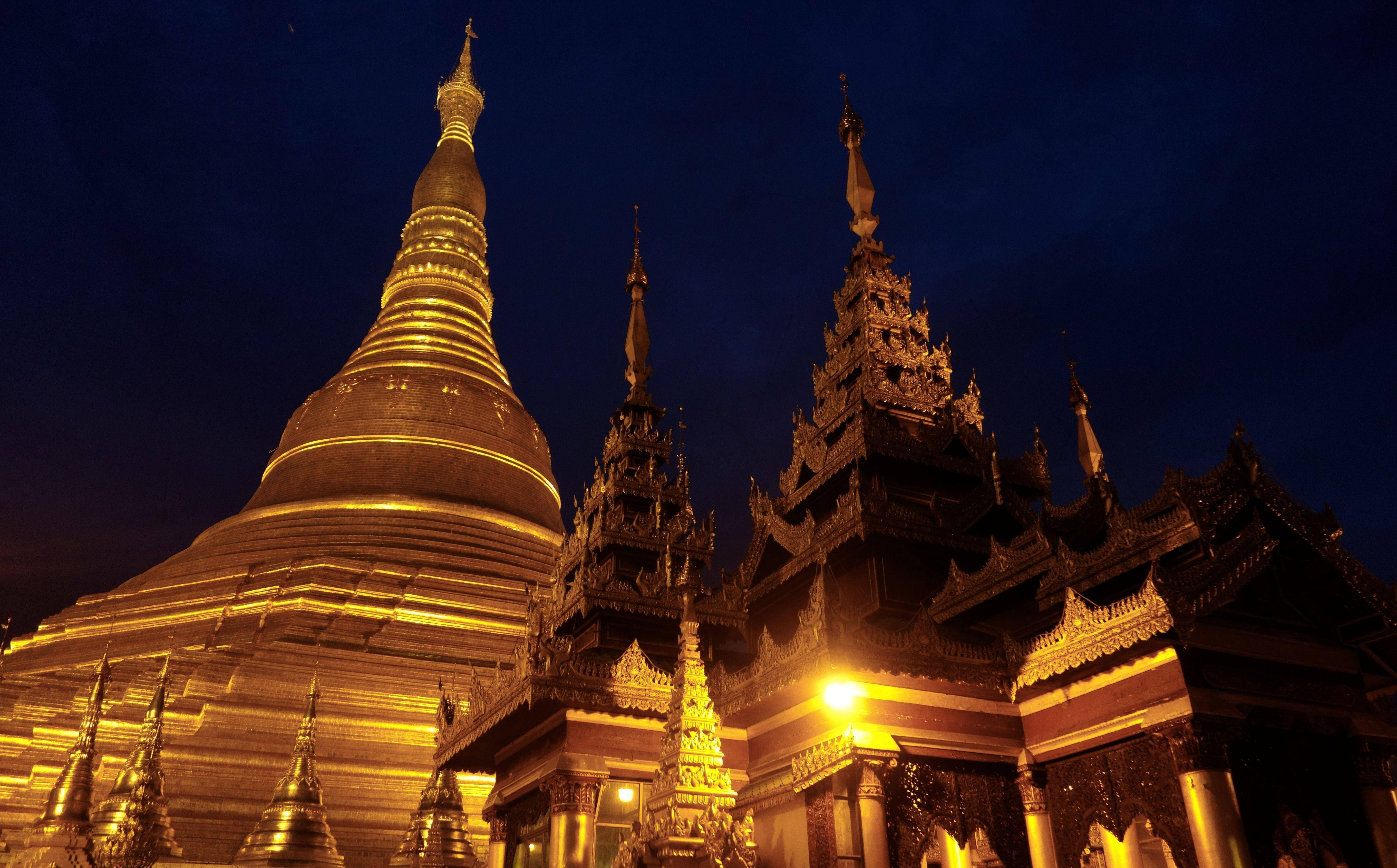 Burma 桌布 壁紙 — 金色佛塔在深藍色夜空下溫暖地發光，位於寧靜的佛教寺廟建築群中。