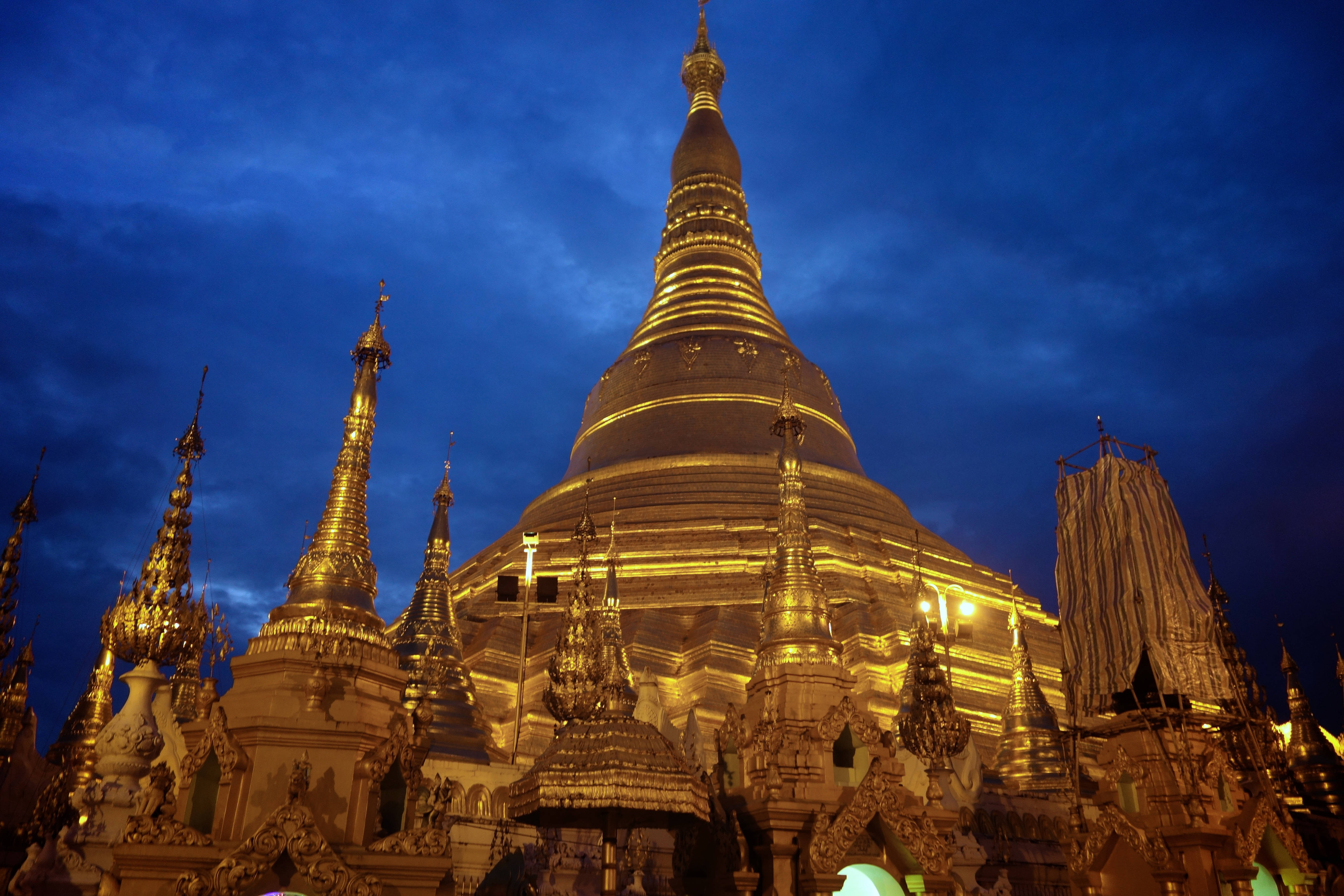 Yangon 桌布 壁紙 — 金色佛塔尖頂在深藍色暮色天空中溫暖地發光，構成宏偉的佛教寺廟建築群。