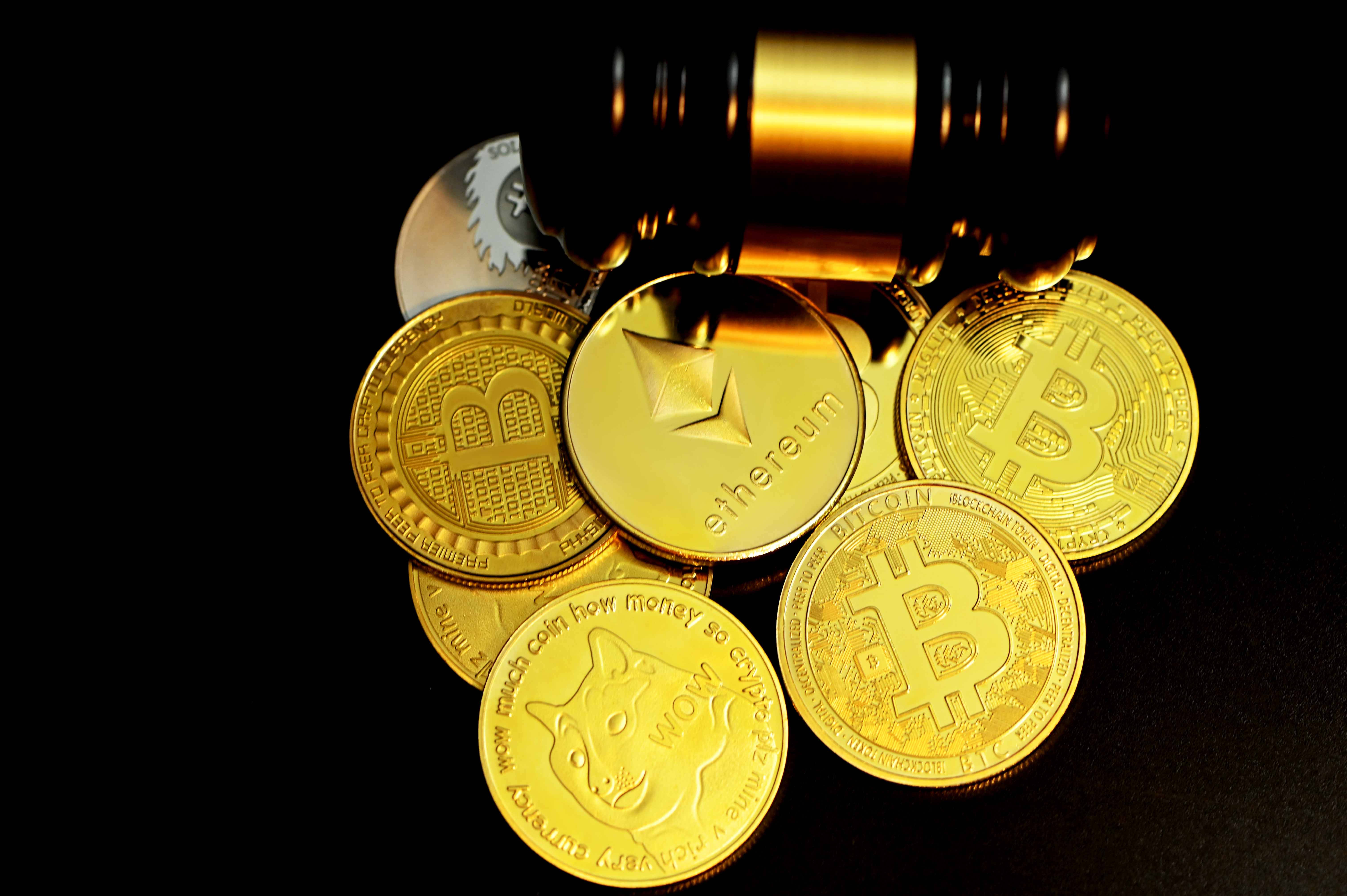 Cryptocurrency 桌布 壁紙 — 金色加密貨幣硬幣，包括比特幣、以太幣和狗狗幣，放在黑色背景上的槌子下。