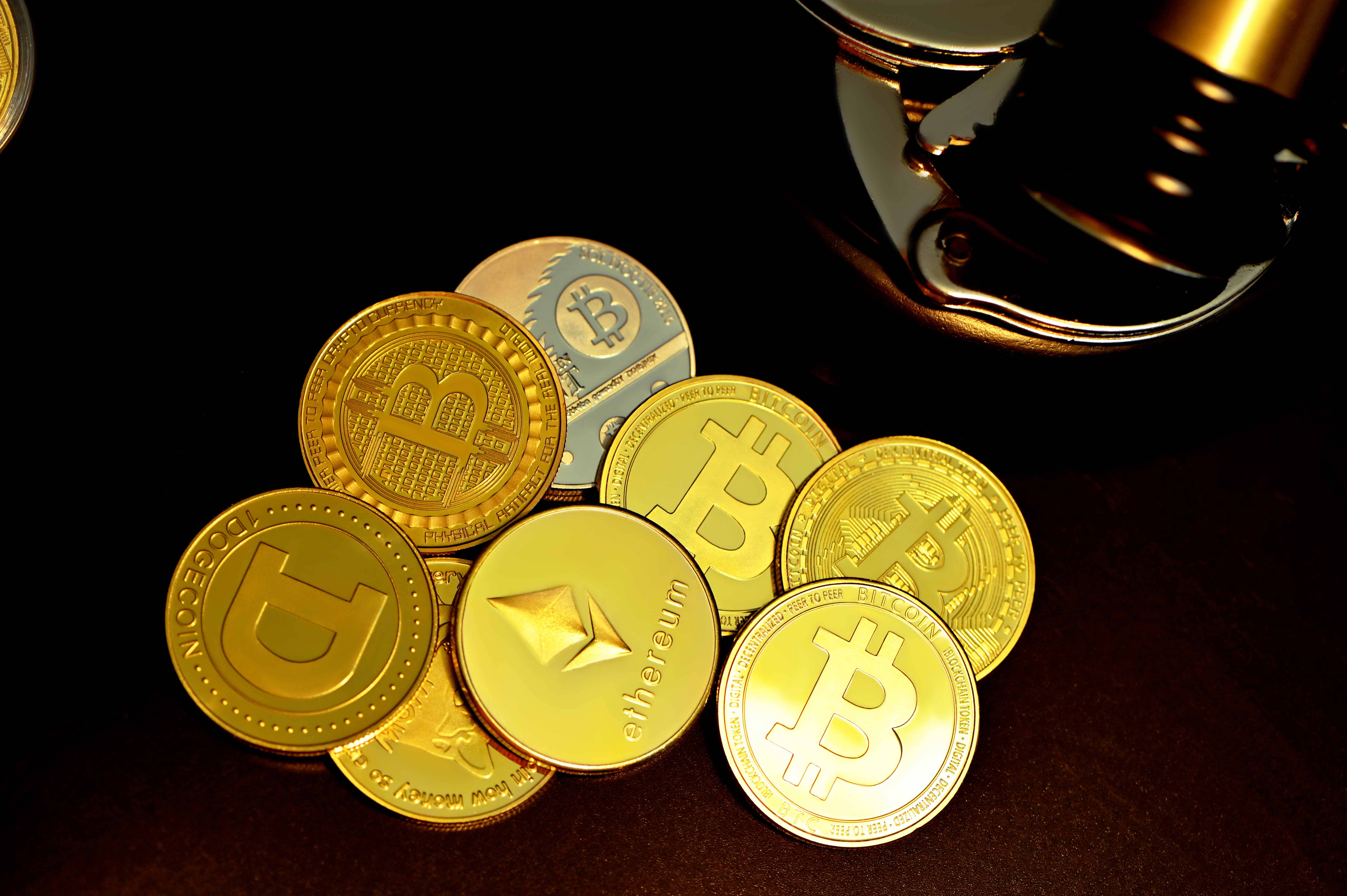 Cryptocurrency 桌布 壁紙 — 金色加密貨幣硬幣（包括比特幣和以太幣）放在深色表面上，旁邊有一個木槌。