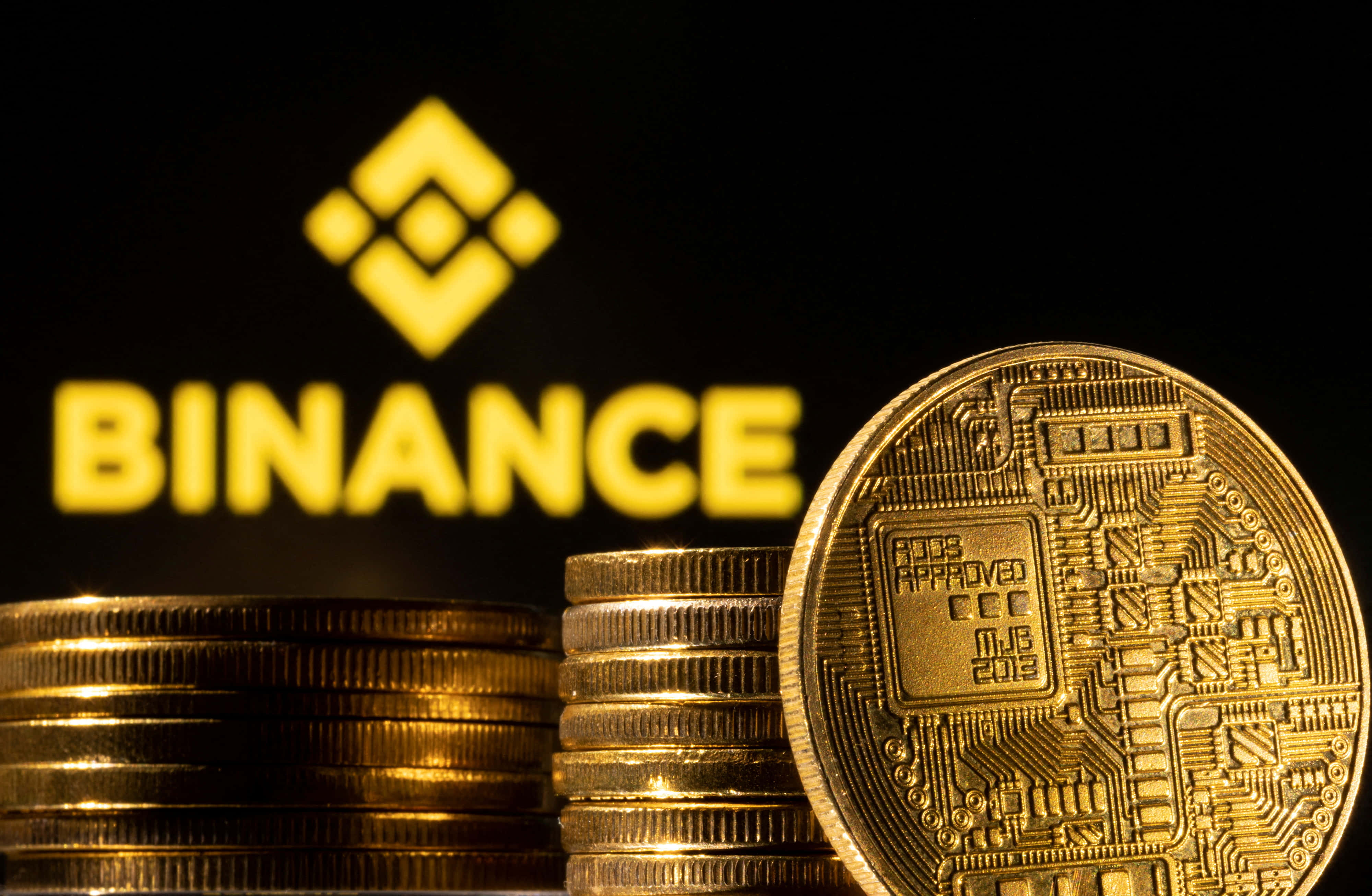 Binance 桌布 壁紙 — 金色加密貨幣硬幣堆疊在黑色背景上發光的 Binance 標誌前。