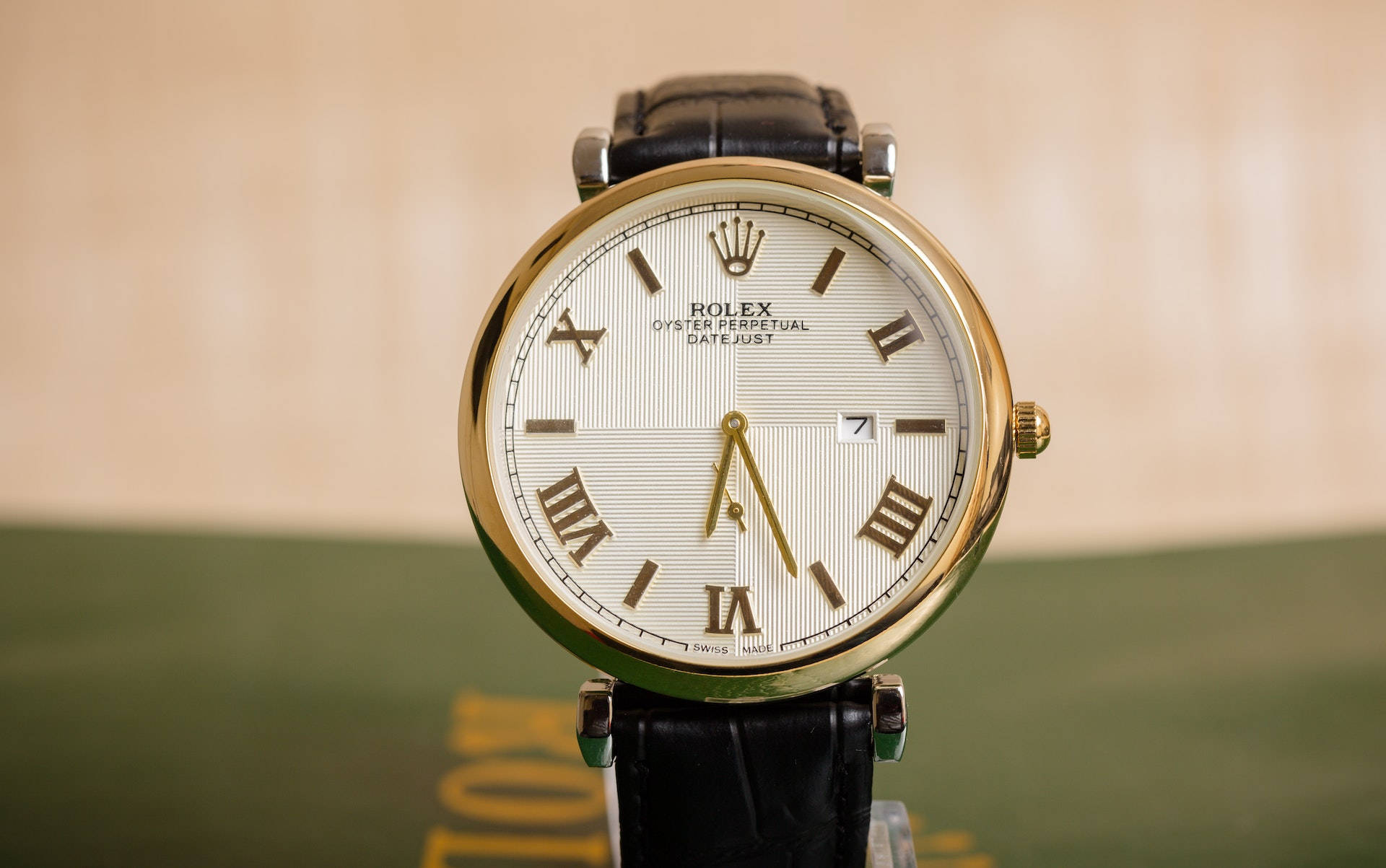 復古 桌布 壁紙 — 金色勞力士Oyster Perpetual Datejust手錶搭配黑色皮革錶帶的特寫，背景為模糊的米色和綠色。