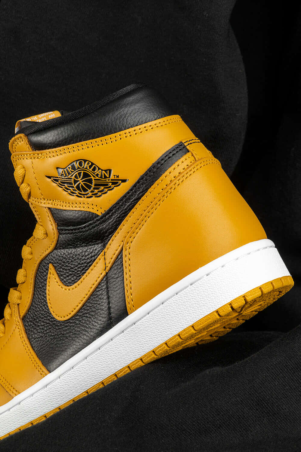 Yellow Jordan 桌布 壁紙 — 金色和黑色 Air Jordan 1 運動鞋特寫，白色鞋底，深色布料背景。