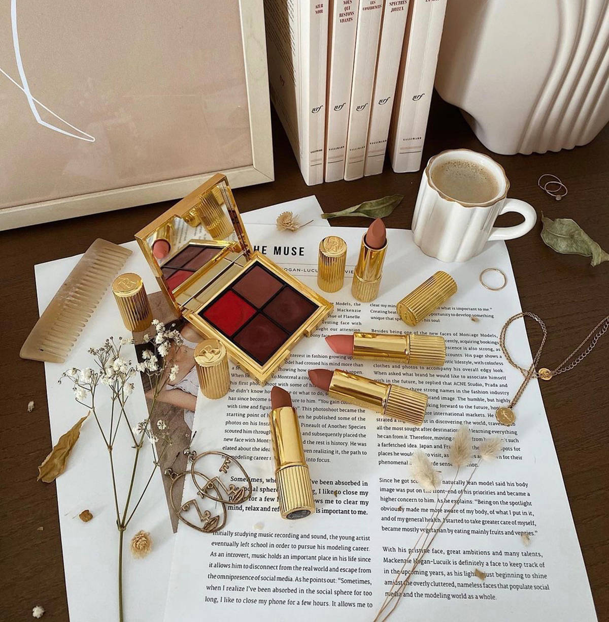 彩妝 桌布 壁紙 — 金色唇膏管和化妝刷優雅地放在打開的書頁上，旁邊是一個白色馬克杯和乾花，在木桌上。