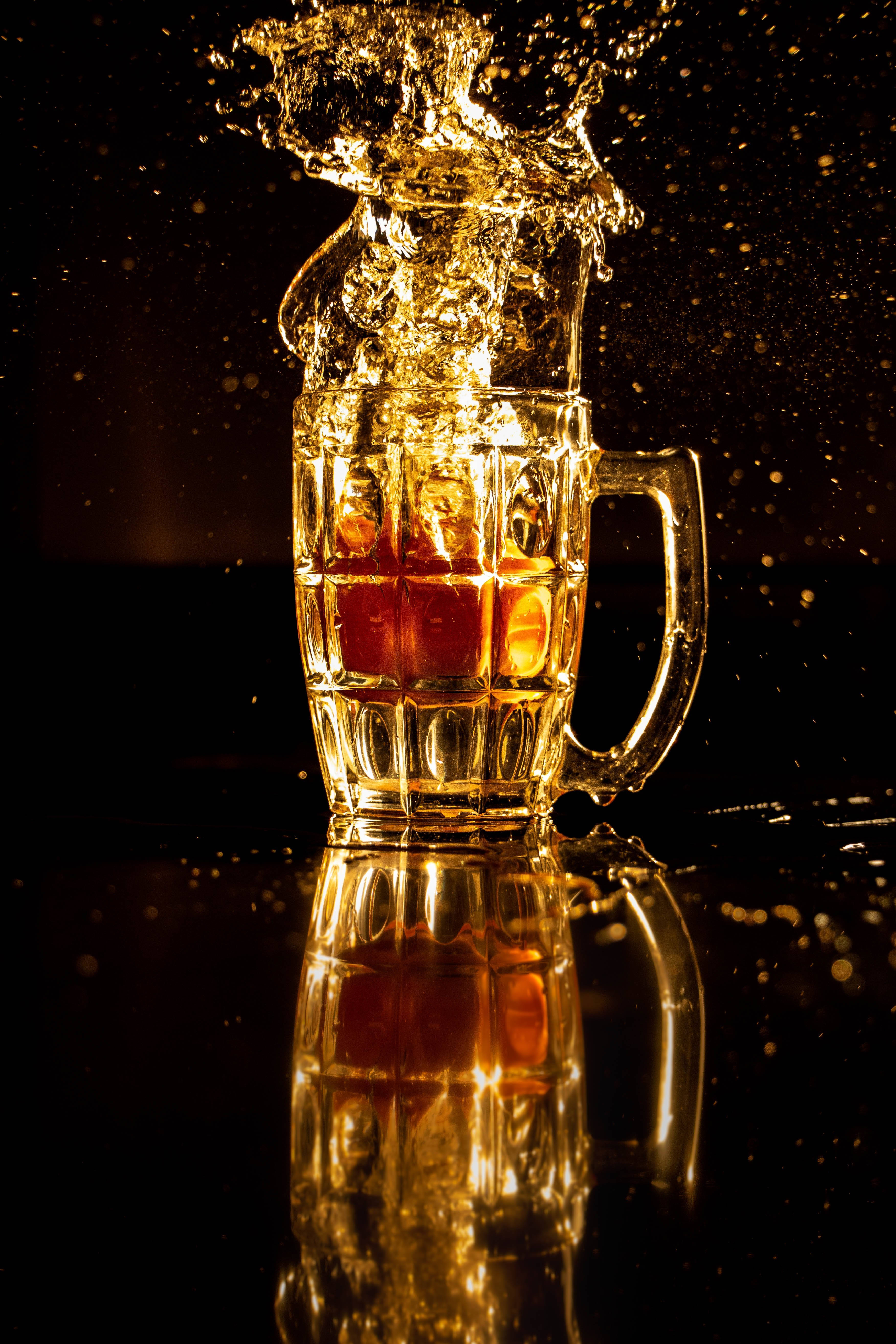Cheers 桌布 壁紙 — 金色啤酒從有紋理的玻璃杯戲劇性地濺出，落在深色反光表面上。