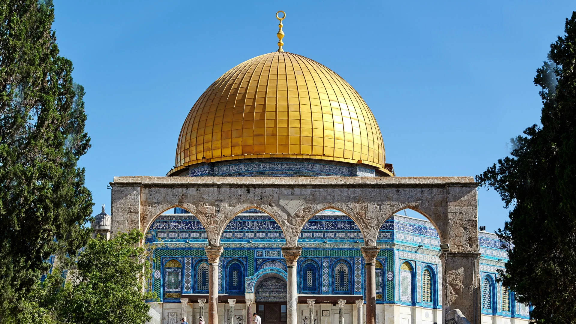 muslim 桌布 壁紙 — 金色圓頂岩石在晴朗藍天下閃耀，四周環繞著茂密的綠樹。