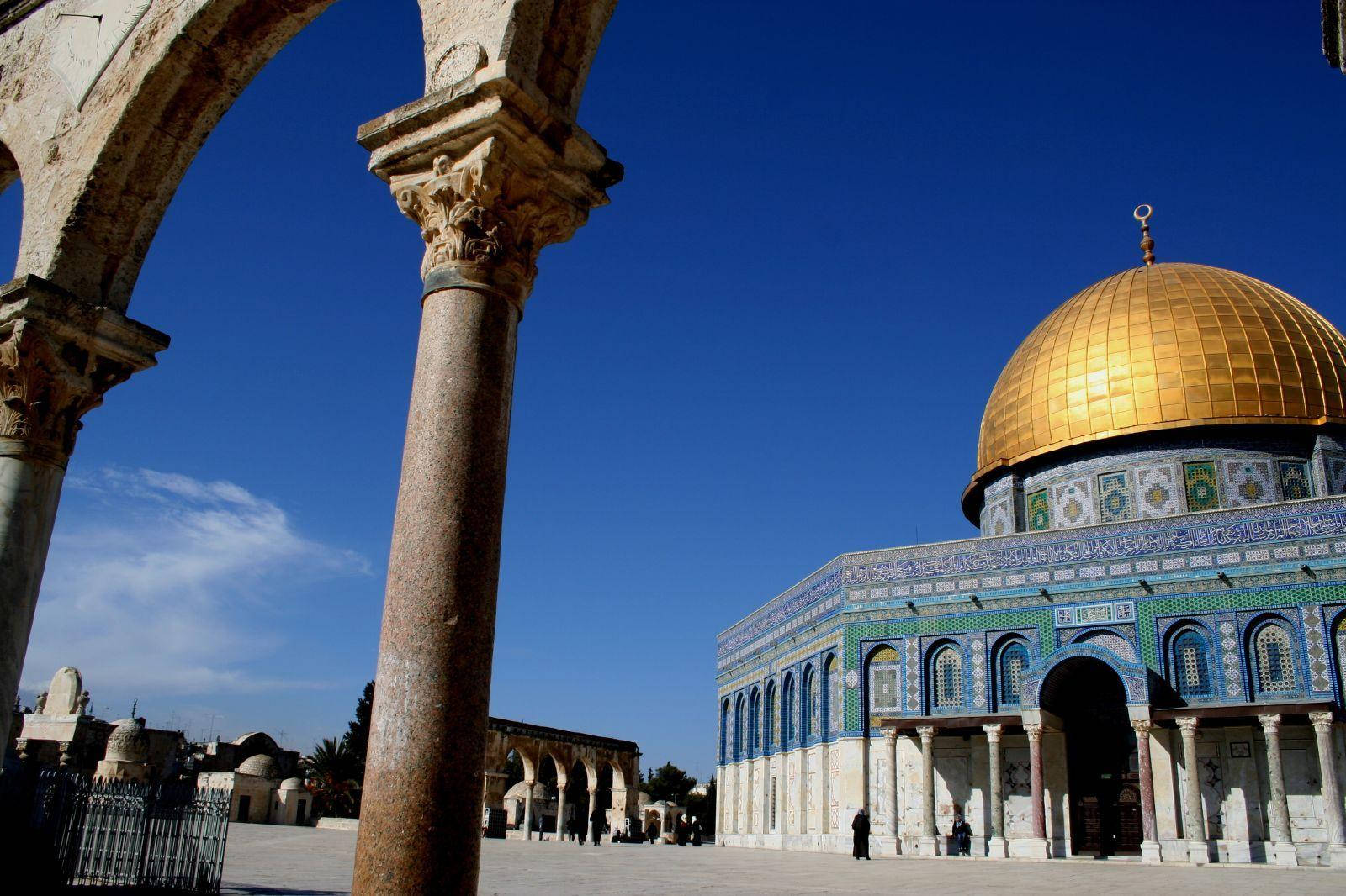 muslim 桌布 壁紙 — 金色圓頂岩石在清澈藍天下閃耀，被古老石拱門和柱子框住。