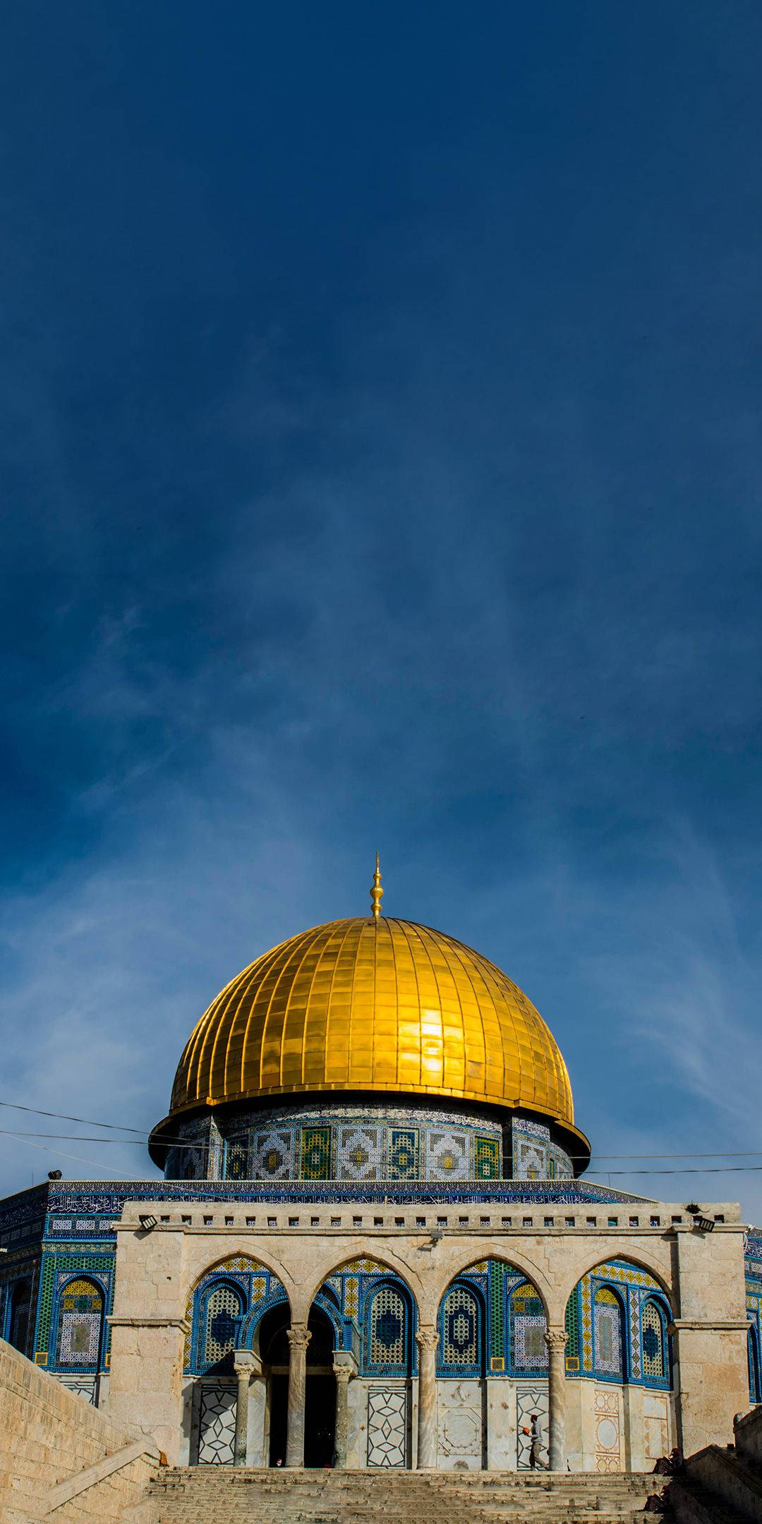 muslim 桌布 壁紙 — 金色圓頂清真寺在清澈藍天下閃耀，下方有精緻的藍色瓷磚和石拱門。