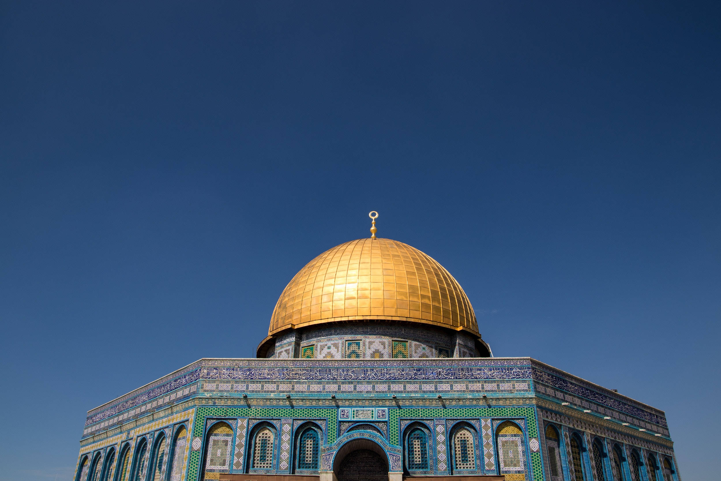 muslim 桌布 壁紙 — 金色圓頂清真寺在清澈藍天下閃耀，下方有精緻的藍色瓷磚工藝。