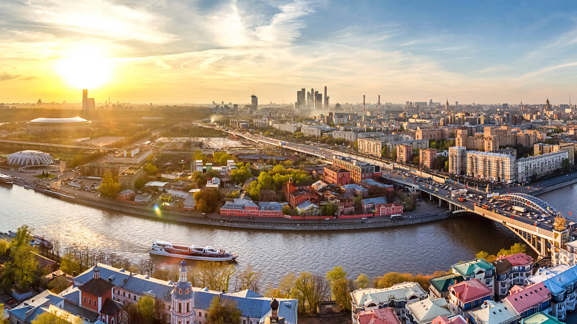 Russia 桌布 壁紙 — 金色夕陽下廣闊城市景觀的鳥瞰圖，蜿蜒的河流和橋樑連接歷史與現代建築。