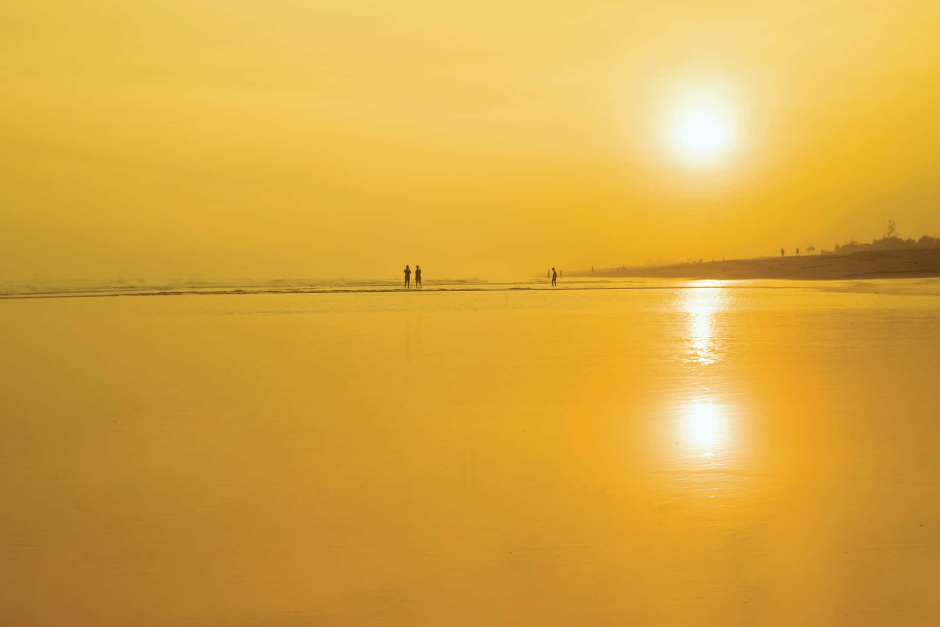 Yellow Beach 桌布 壁紙 — 金色夕陽以溫暖光線沐浴廣闊濕沙灘，剪影人物在水平線附近漫步。