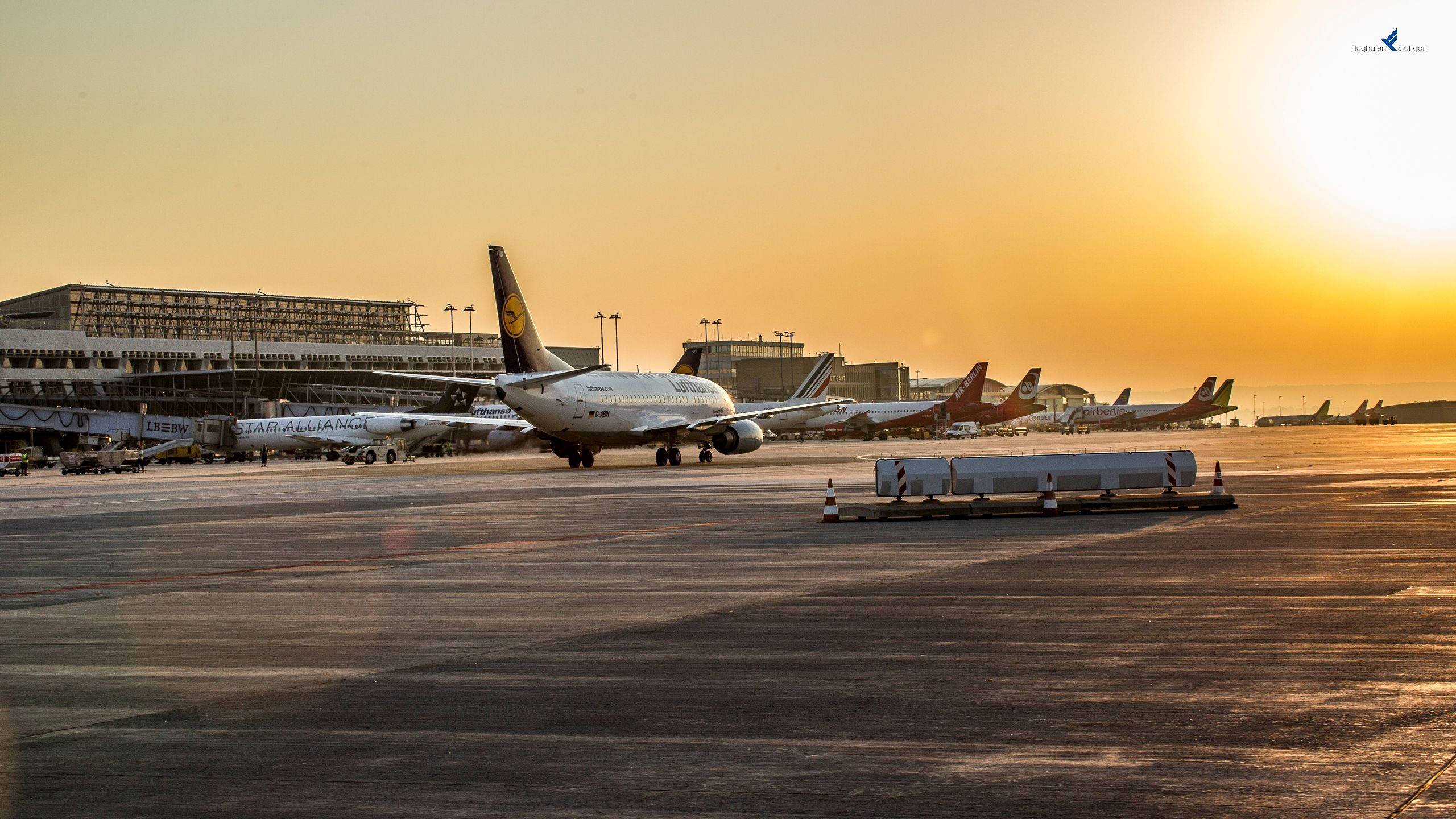 Airport 桌布 壁紙 — 金色夕陽以溫暖光線沐浴機場停機坪，飛機在閘口休息，背景是航廈建築。