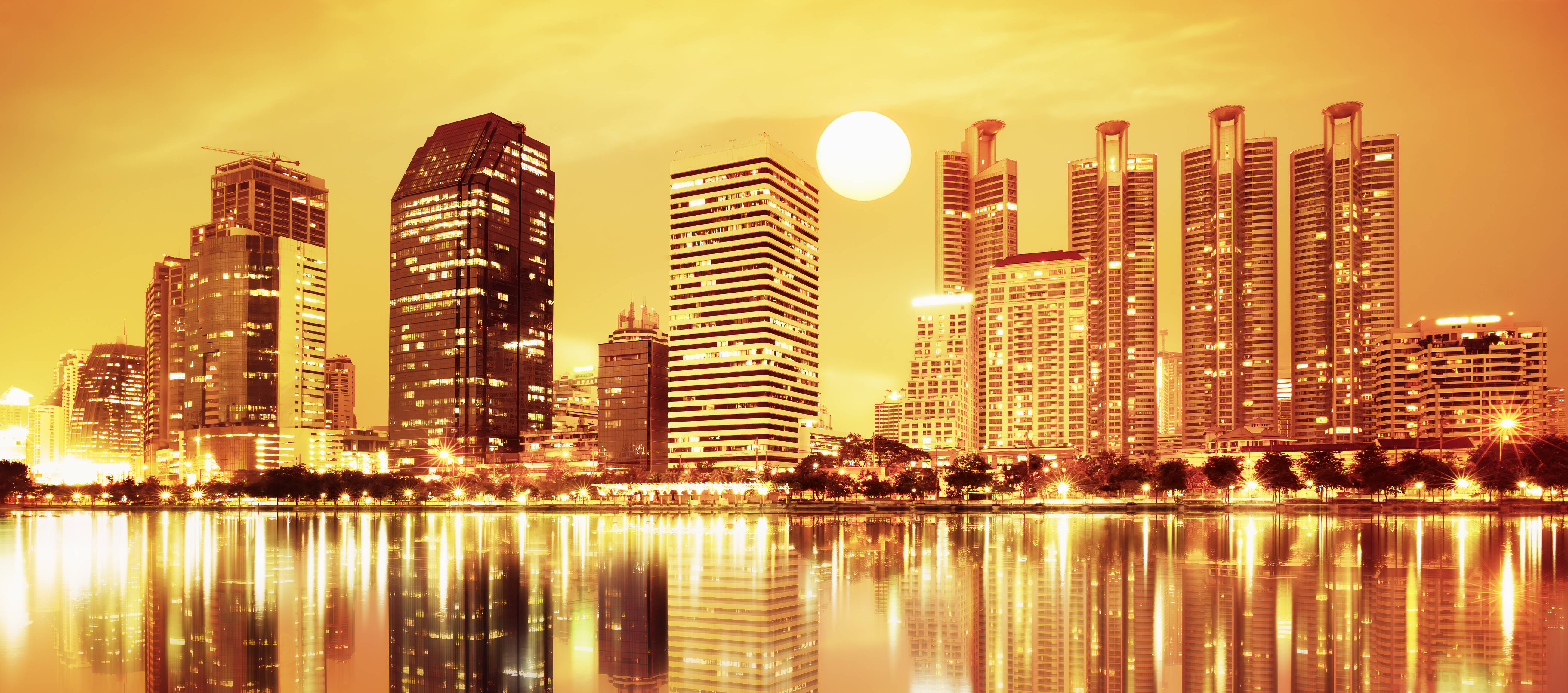 Orange City 桌布 壁紙 — 金色夕陽以溫暖光線沐浴現代摩天大樓，它們的倒影在下方平靜水面上閃爍。