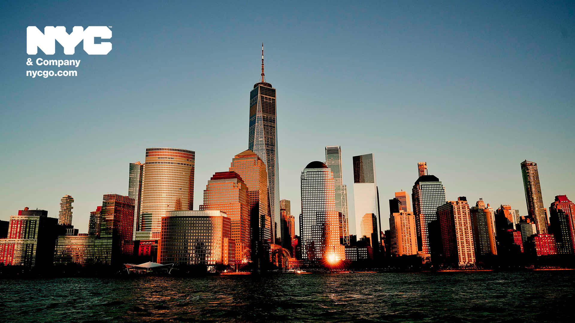 New York 桌布 壁紙 — 金色夕陽以溫暖光線沐浴著紐約市標誌性的天際線，並倒映在下方水面上。