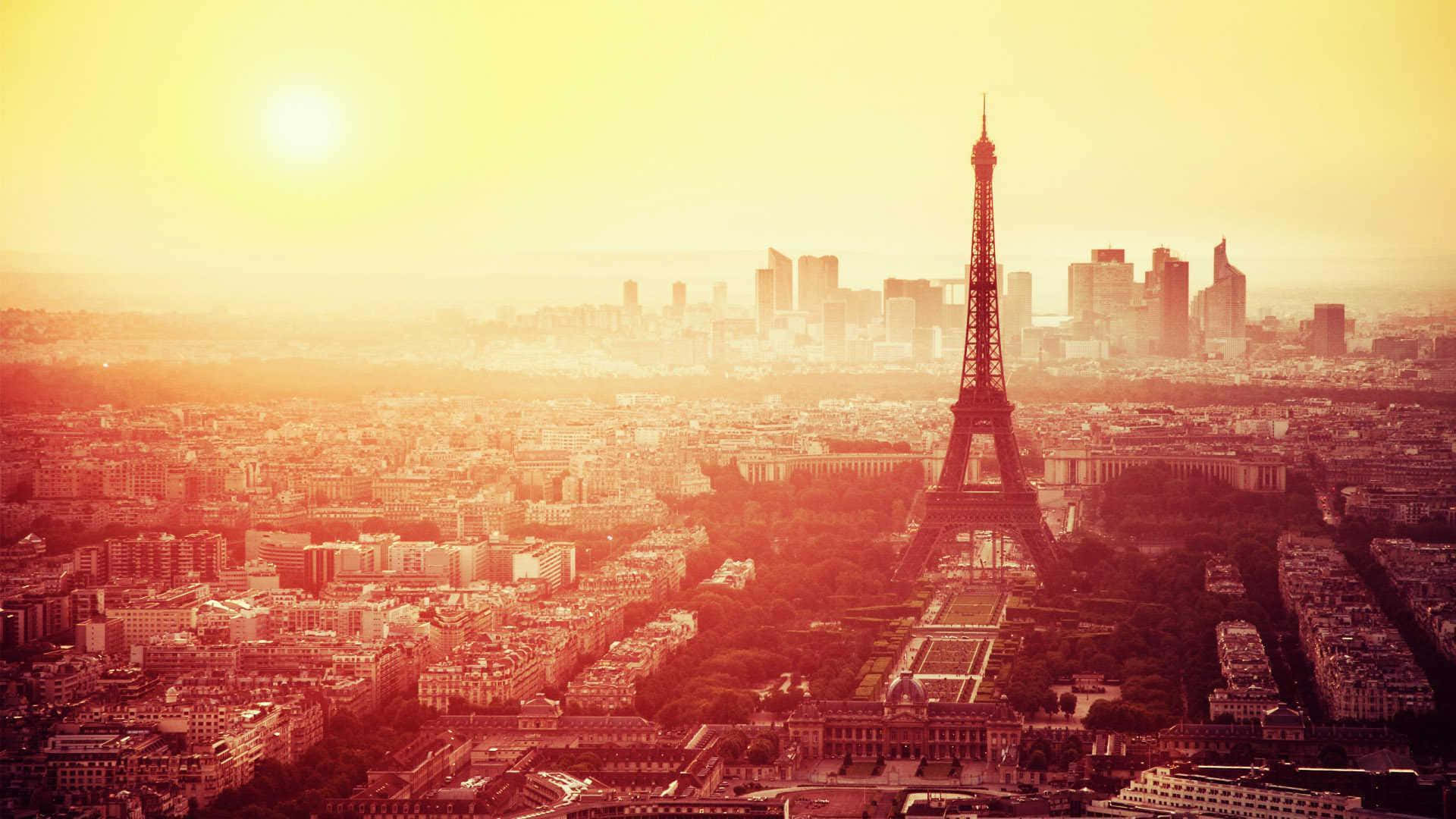 Eiffel Tower 桌布 壁紙 — 金色夕陽以溫暖的琥珀色光芒沐浴艾菲爾鐵塔和巴黎天際線，帶有朦朧的大氣光暈。