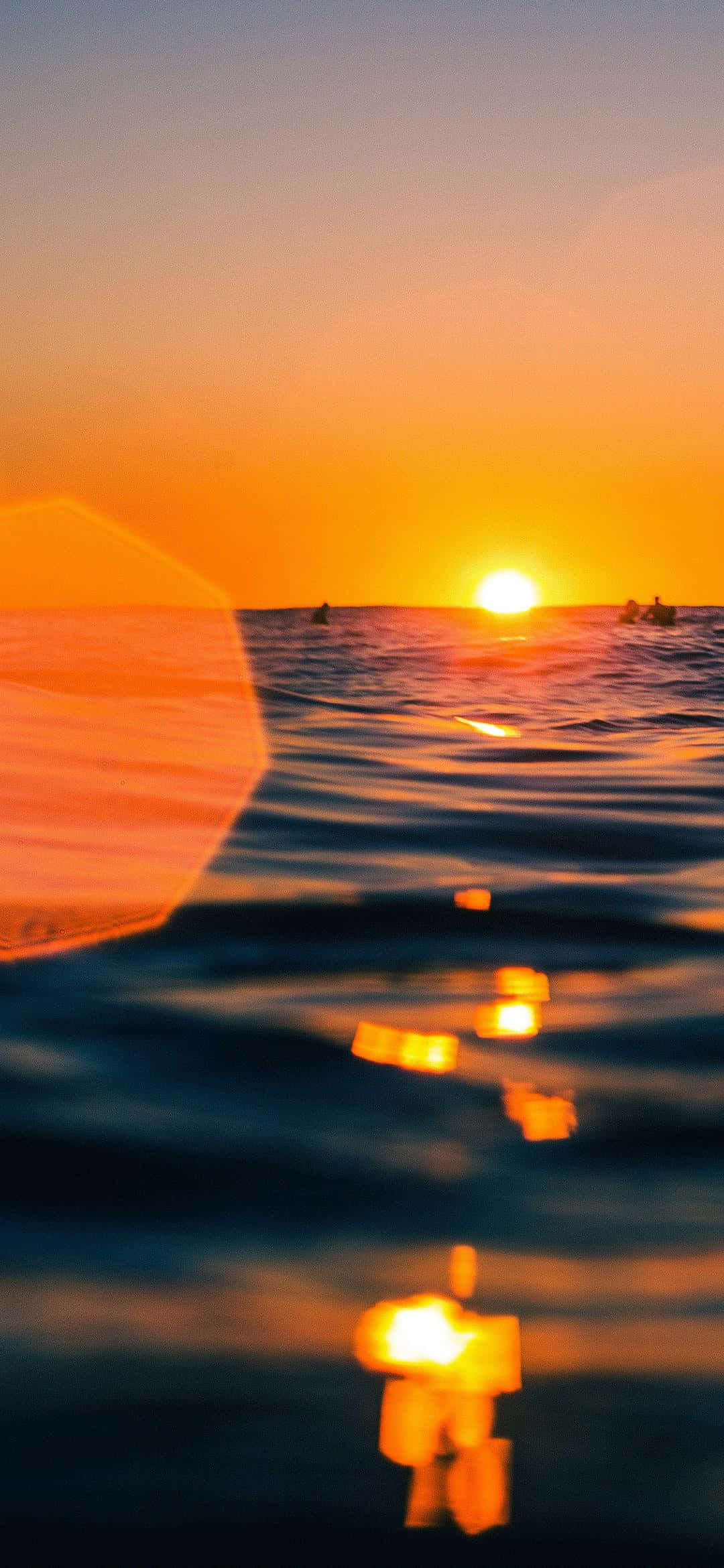 日出 桌布 壁紙 — 金色夕陽在平靜的海浪上閃耀，衝浪者的剪影和鏡頭光暈增添了溫暖。