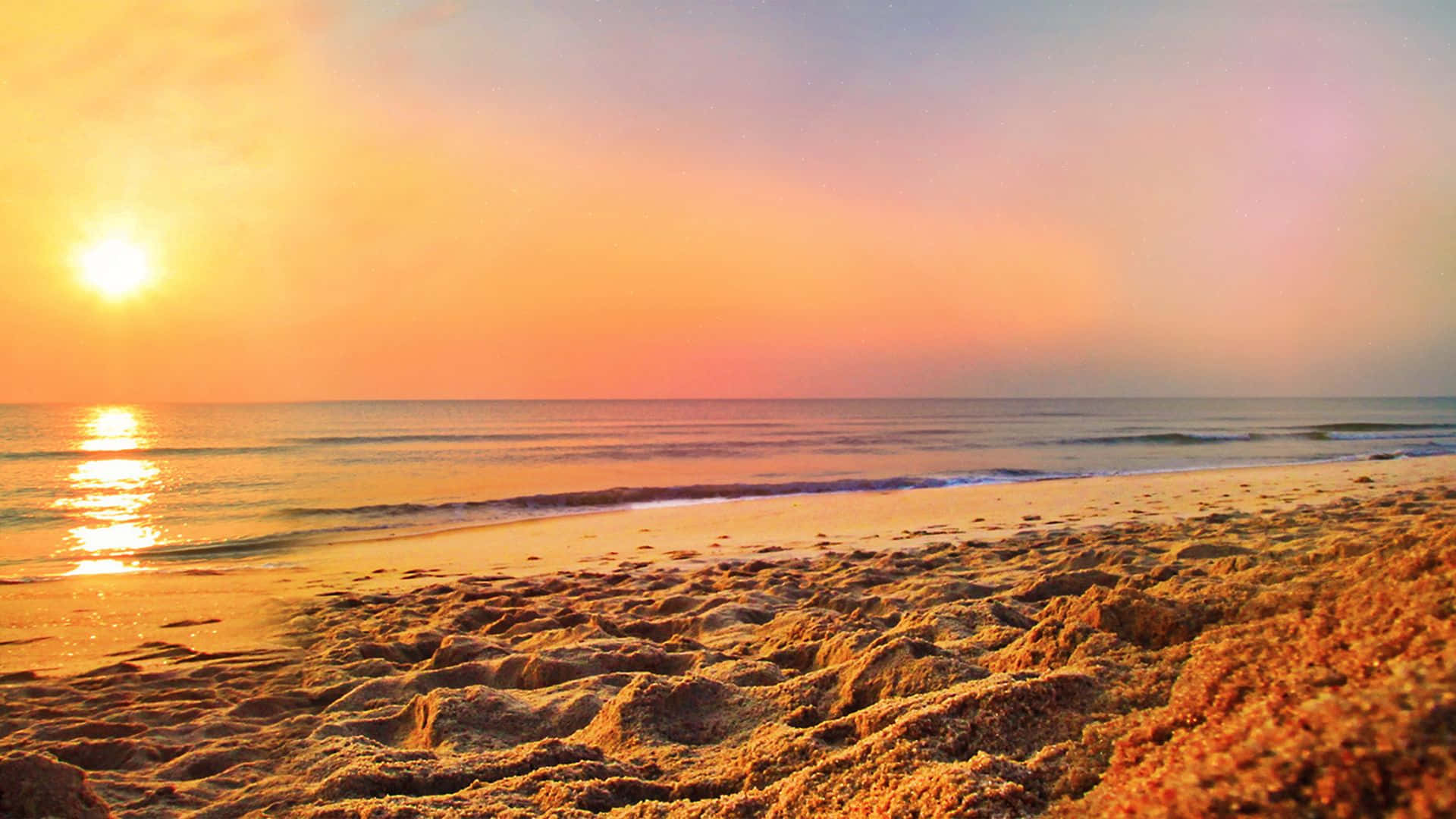 Coastal Sunset 桌布 壁紙 — 金色夕陽在平靜的海浪拍打著質感沙灘上投下溫暖色調。