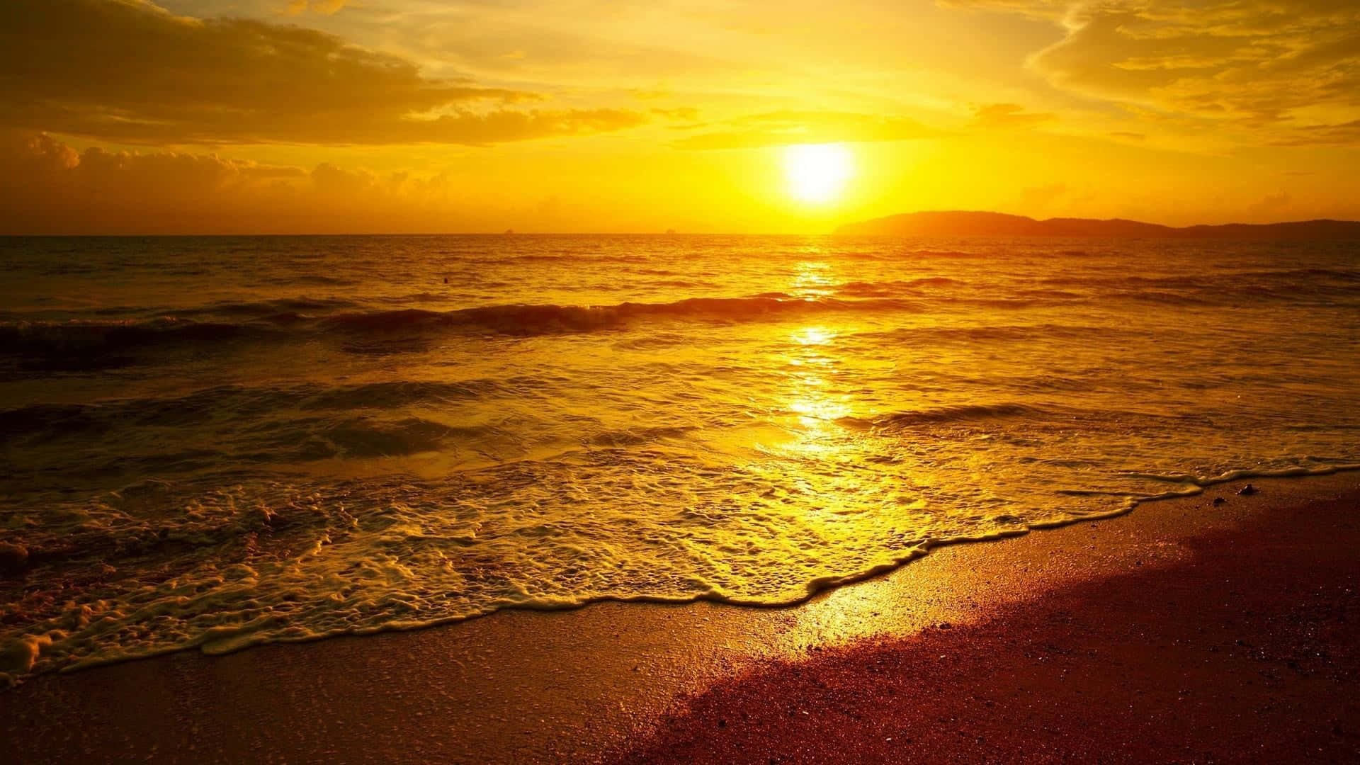 海灘日落 桌布 壁紙 — 金色夕陽將溫暖光線投射在拍打沙灘的海浪上，遠山形成剪影。