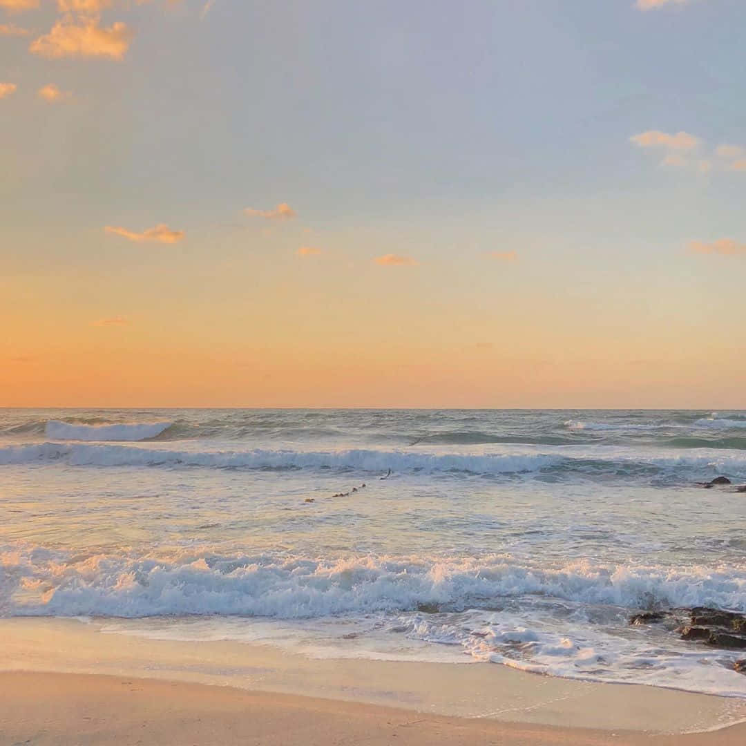 Beach Aesthetic 桌布 壁紙 — 金色夕陽描繪著海浪拍打沙灘，在柔和粉彩天空下。