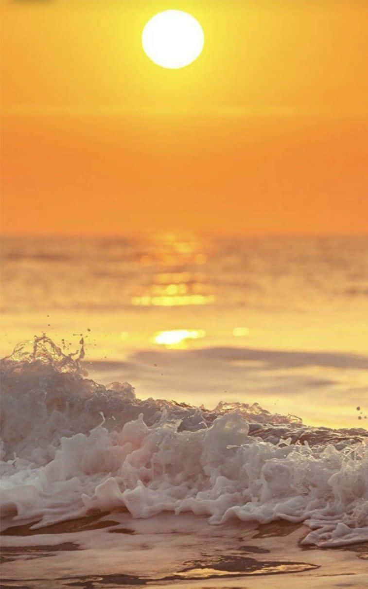 Yellow Sky 桌布 壁紙 — 金色夕陽映照海洋波浪，拍打沙灘，呈現溫暖的橙色和黃色色調。