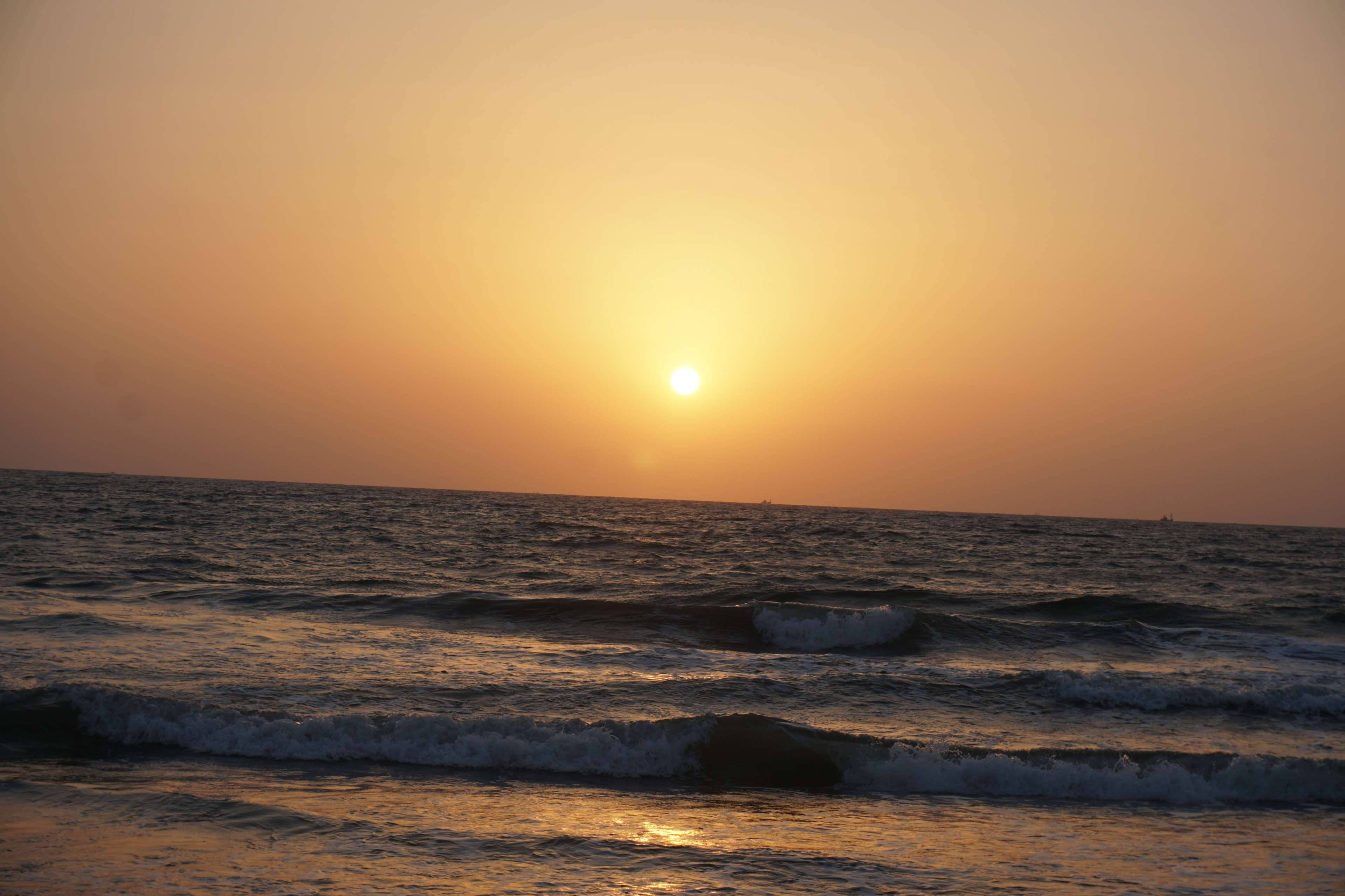 夕陽天空 桌布 壁紙 — 金色夕陽沉入地平線下，在平靜的日落中為翻滾的海浪投下溫暖的光芒。