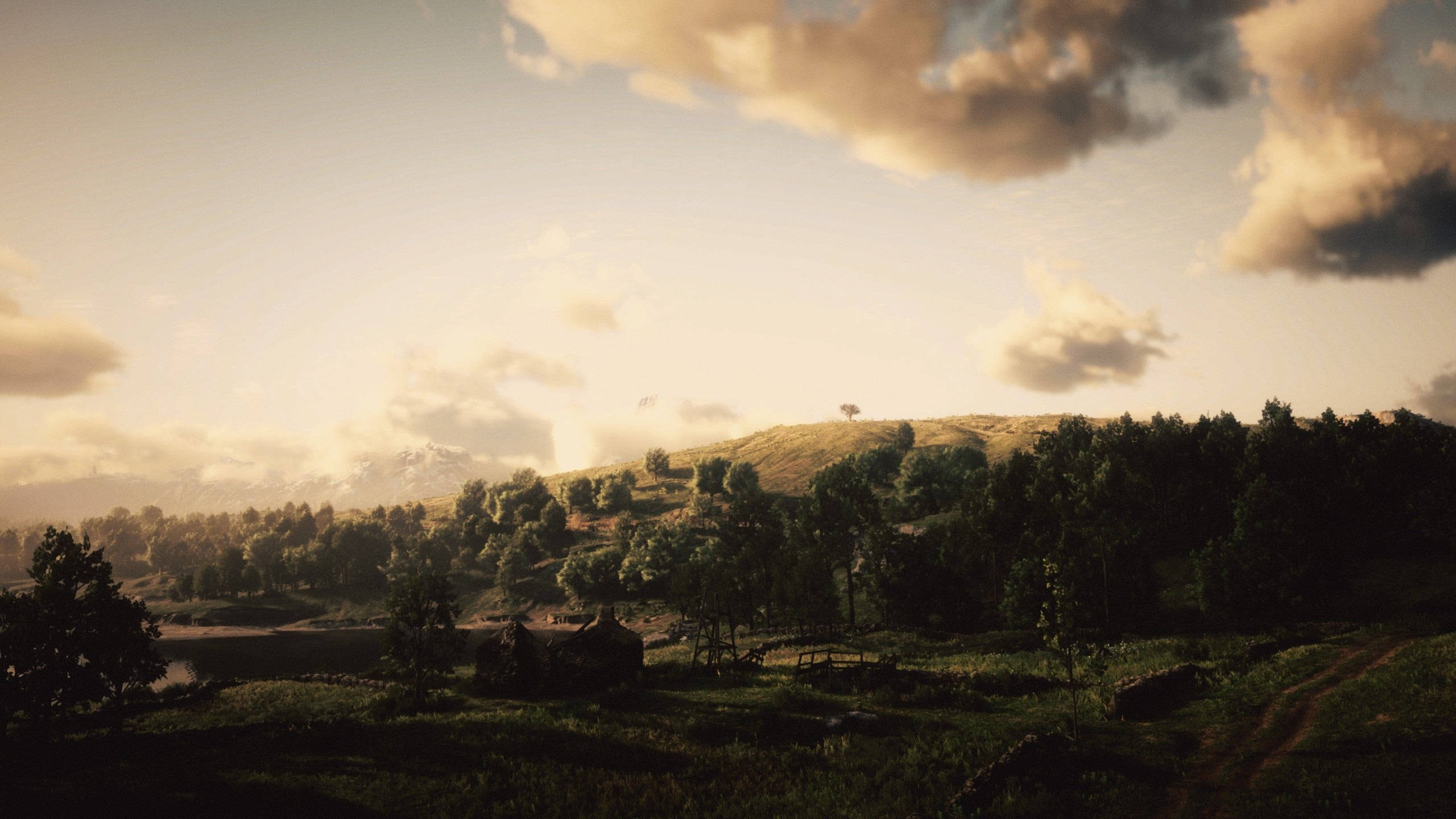 Red Dead Redemption 2 Desktop 桌布 壁紙 — 金色夕陽沐浴著寧靜的山谷，有起伏的丘陵、樹木和遠處白雪覆蓋的山脈，在柔軟的雲層下。