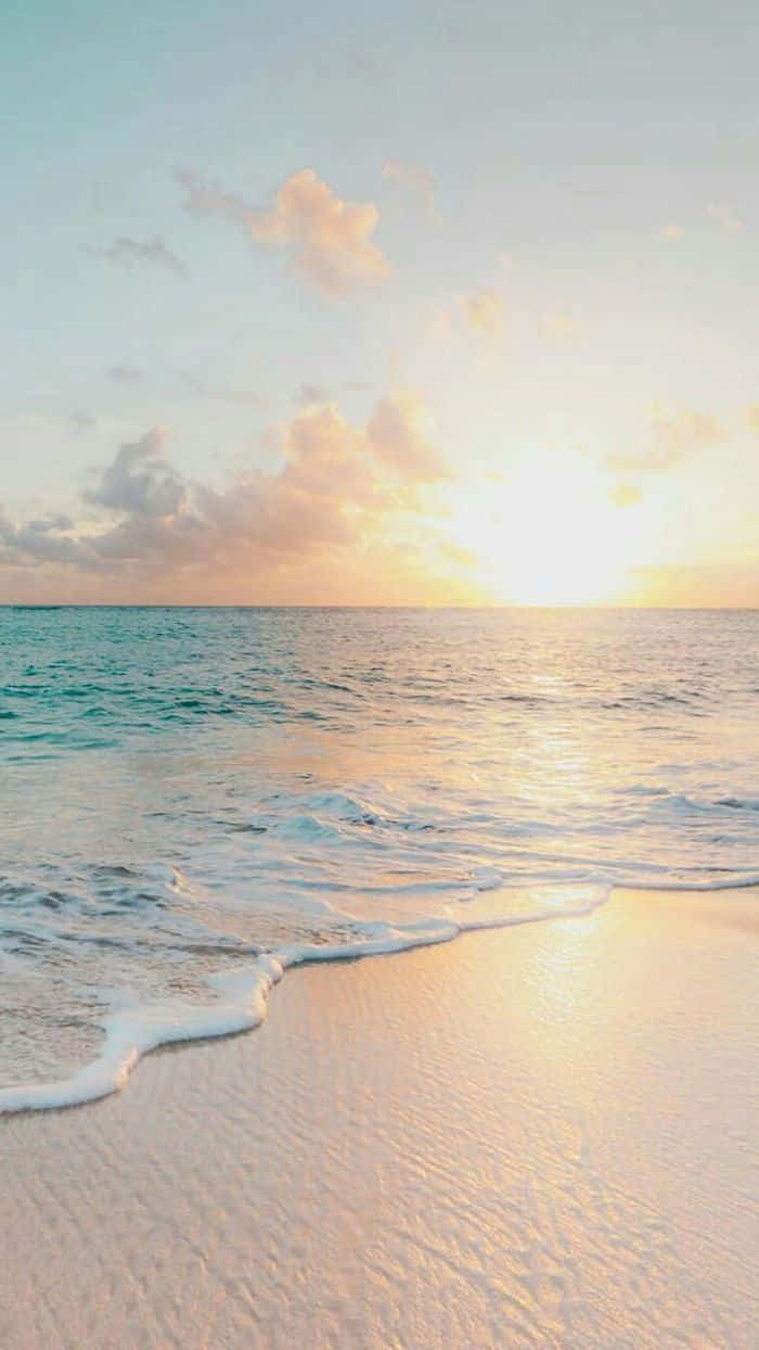 Cute Beach iPhone 桌布 壁紙 — 金色夕陽海浪輕輕拍打柔軟沙灘，天空是粉彩色的，散落著雲朵。