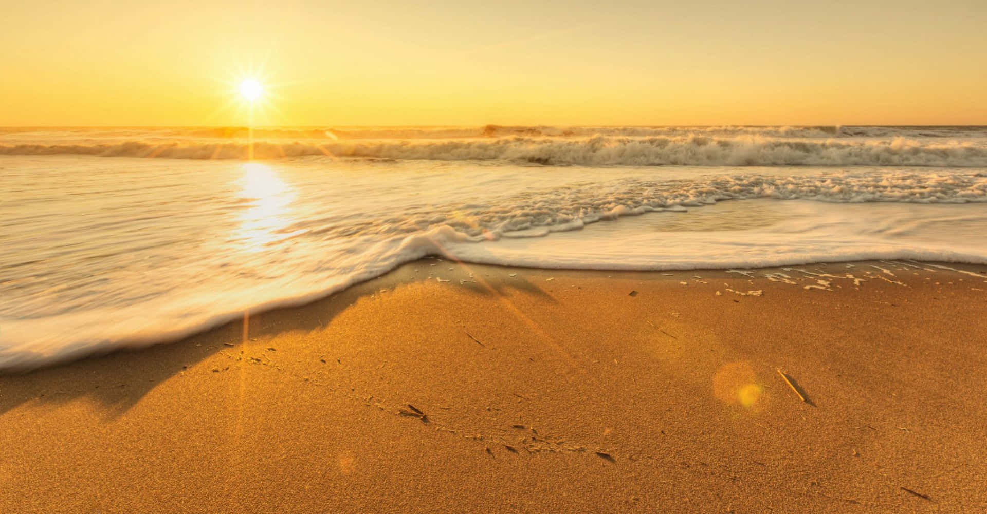 Sunny Day 桌布 壁紙 — 金色夕陽海浪輕輕拍打溫暖沙灘，帶有鏡頭光暈和柔軟泡沫。
