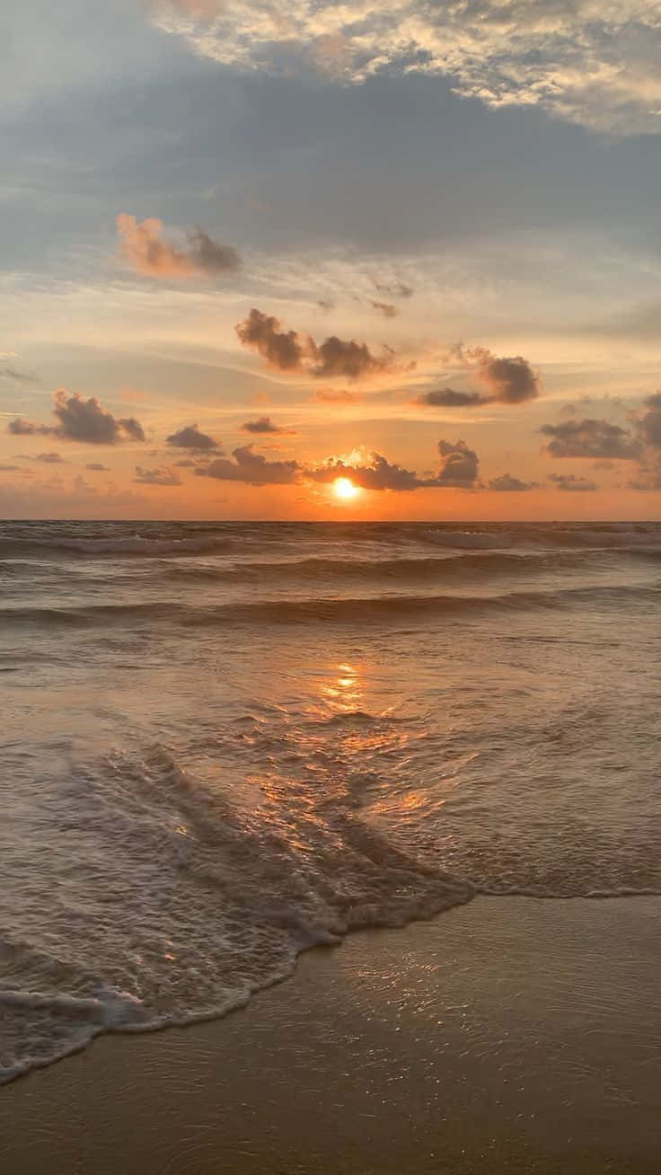 海灘 桌布 壁紙 — 金色夕陽照耀在帶有零星雲朵的沙灘上翻滾的海浪上。