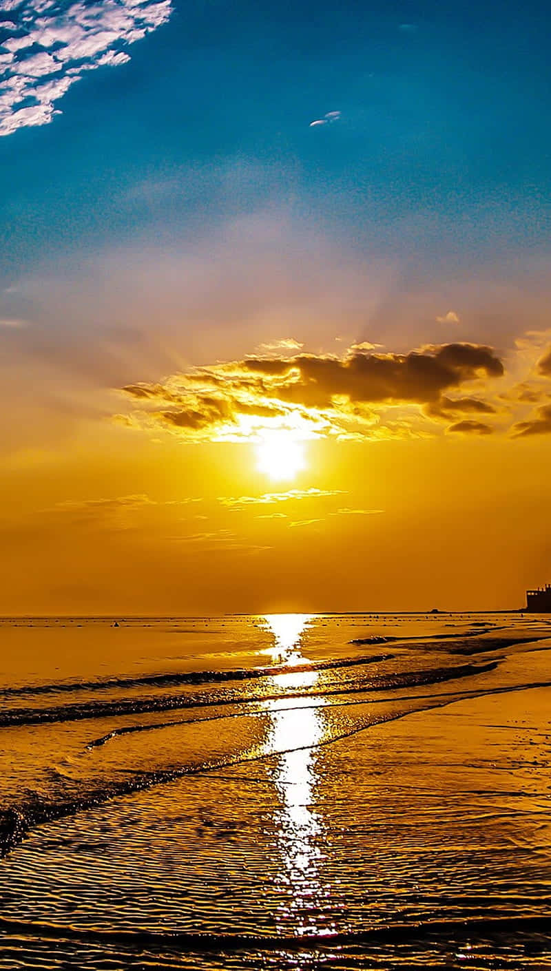 太陽 桌布 壁紙 — 金色夕陽照耀在平靜的海浪上，反射出耀眼的光芒在濕沙上，藍天下有散落的雲朵。