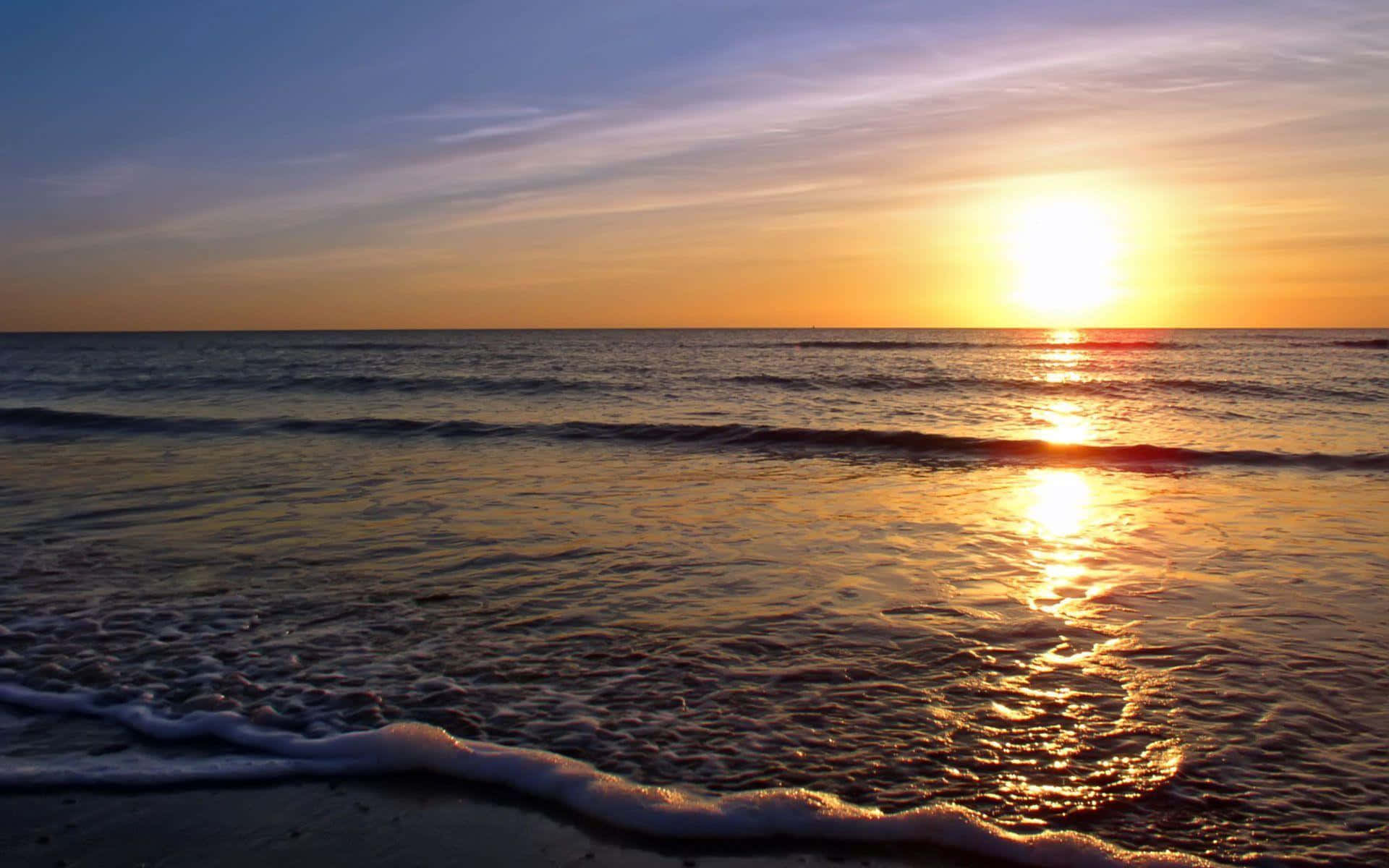桌布 壁紙 — 金色夕陽照耀在平靜的海浪上，帶著柔軟的泡沫沖刷到沙灘上。