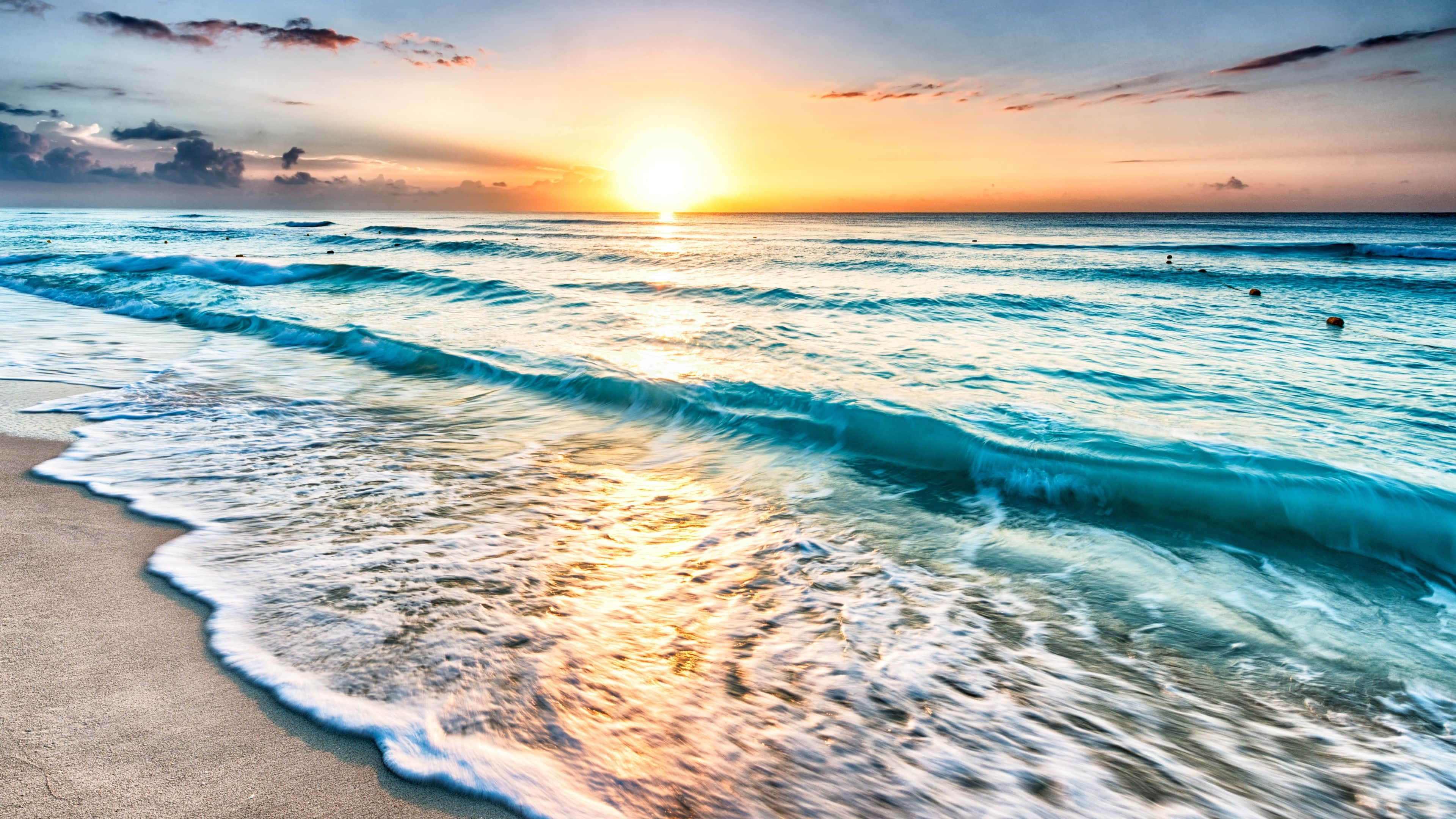 4K Display 桌布 壁紙 — 金色夕陽照耀在碧綠的海浪上，海浪拍打著沙灘，天空中有散落的雲朵。