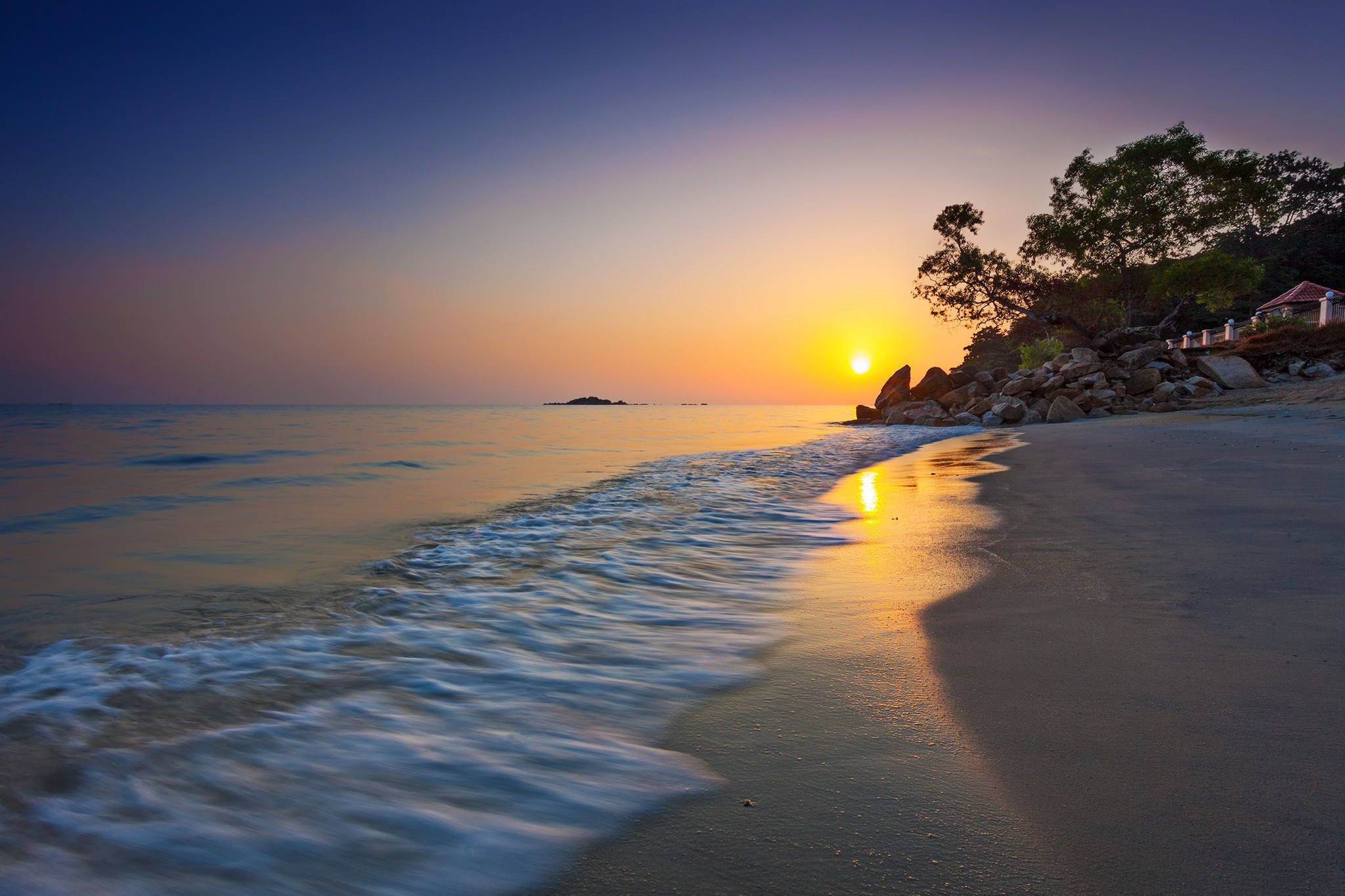 Malaysia 桌布 壁紙 — 金色夕陽照耀著平靜的海浪沖刷到沙灘上，沿岸有樹木和岩石。