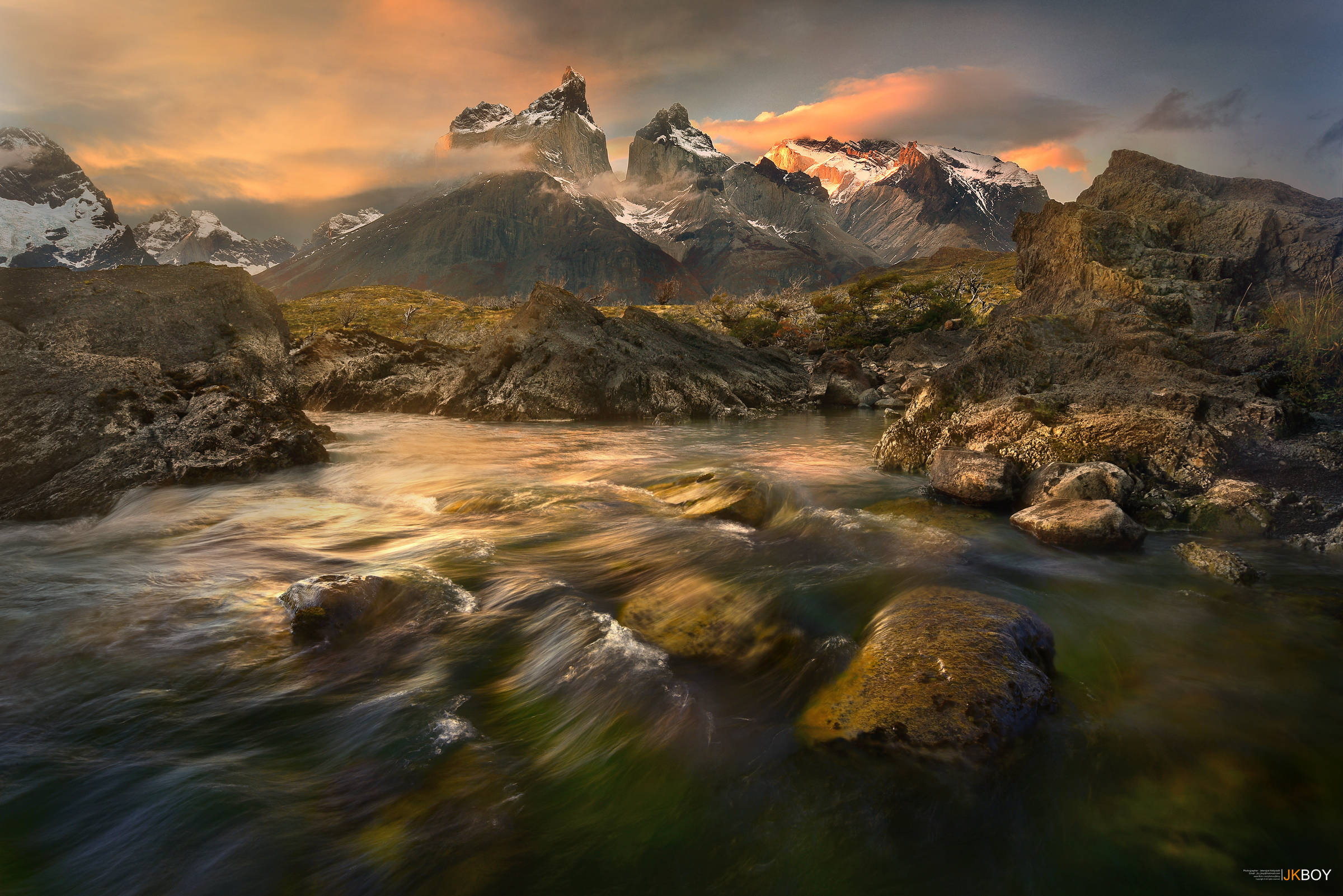 Chile 桌布 壁紙 — 金色夕陽照耀著白雪覆蓋的山峰和流經長滿苔蘚岩石的河流，呈現出戲劇性的阿爾卑斯山景觀。