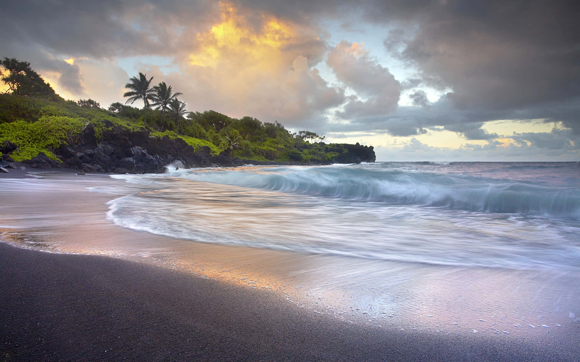Beach Waves 桌布 壁紙 — 金色夕陽穿過暴風雲，照耀在黑色沙灘上，伴隨著拍岸的浪花和翠綠的懸崖。