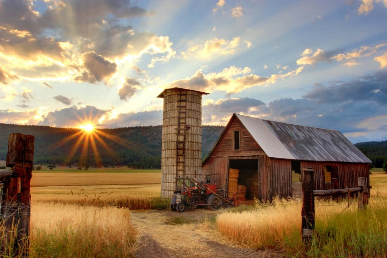 Old Farm 桌布 壁紙 — 金色夕陽穿過雲層，照耀在小麥田中的古樸穀倉和筒倉上。