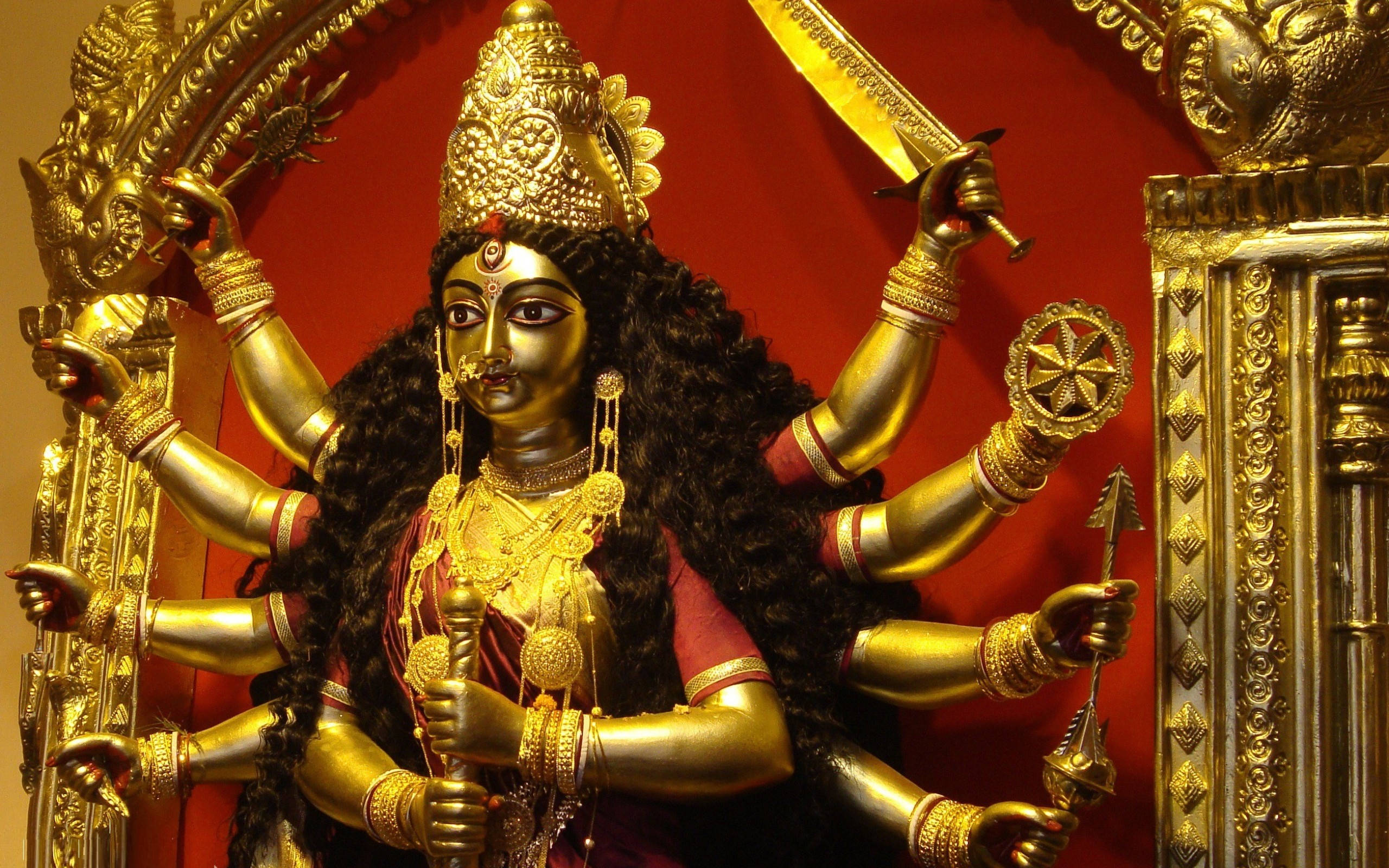Maa Durga 桌布 壁紙 — 金色多臂杜爾迦女神像，手持武器，襯以濃郁的紅色背景。