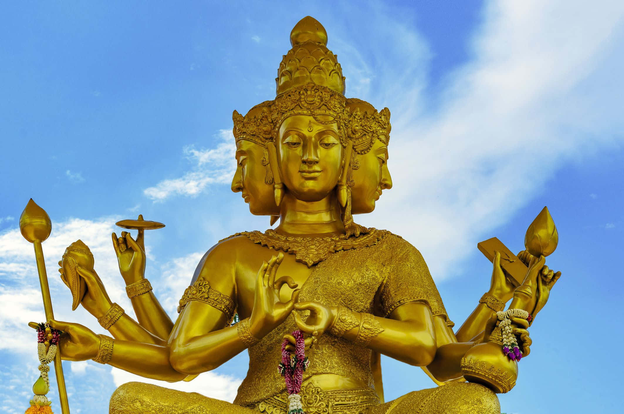 Indian God 桌布 壁紙 — 金色多頭佛像，細節精緻，多隻手持有象徵物品，背景是明亮藍天和縷縷白雲。