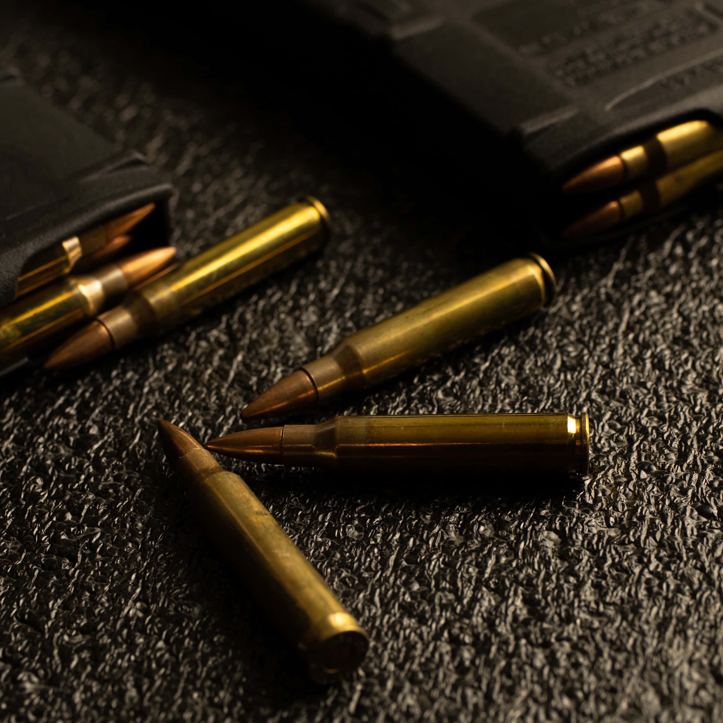 bullet 桌布 壁紙 — 金色子彈放在深色紋理表面上，附近有彈匣，在戲劇性燈光下。