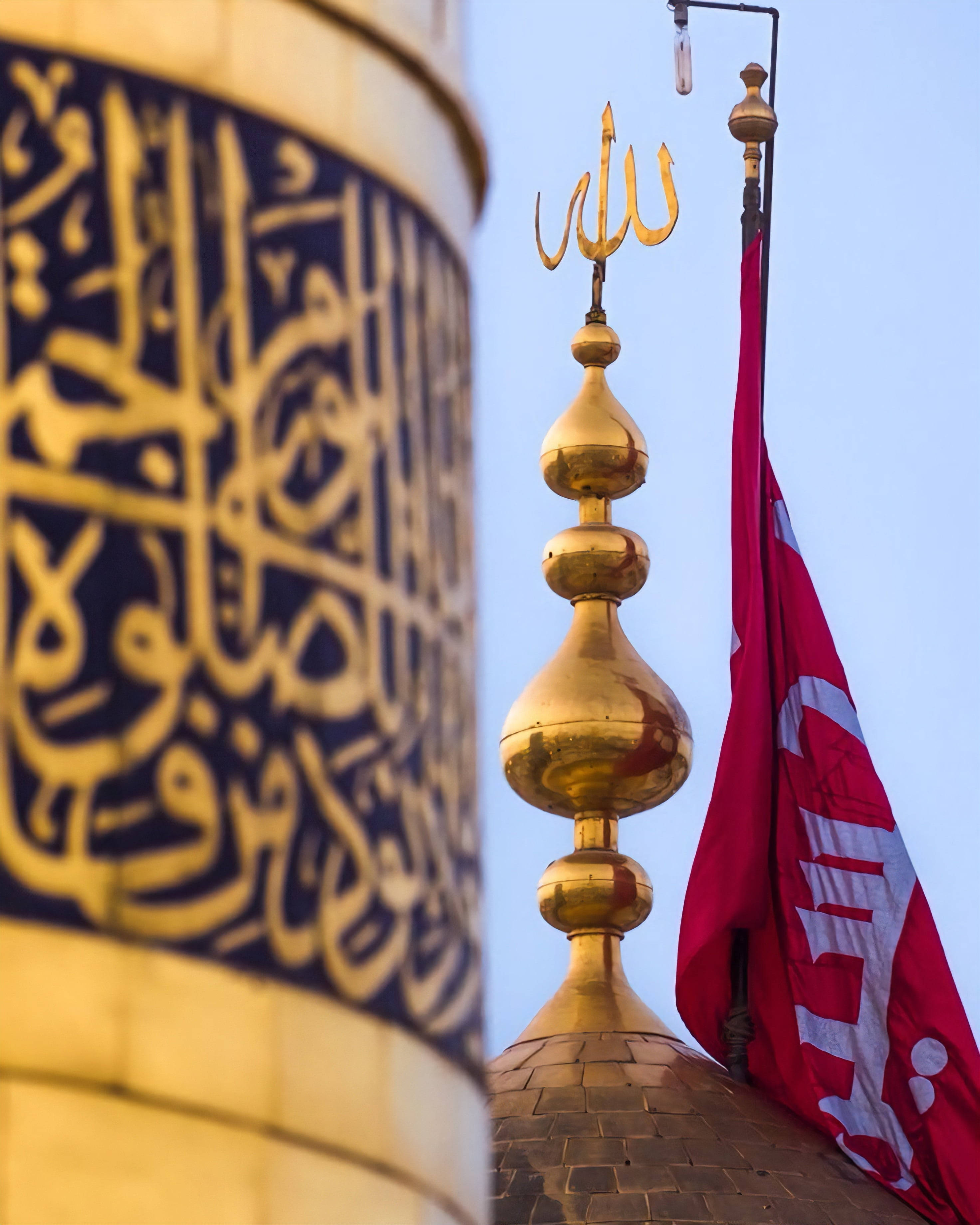 Karbala 桌布 壁紙 — 金色宣禮塔頂和書法風格圓頂在清澈藍天下襯托著一面紅旗。