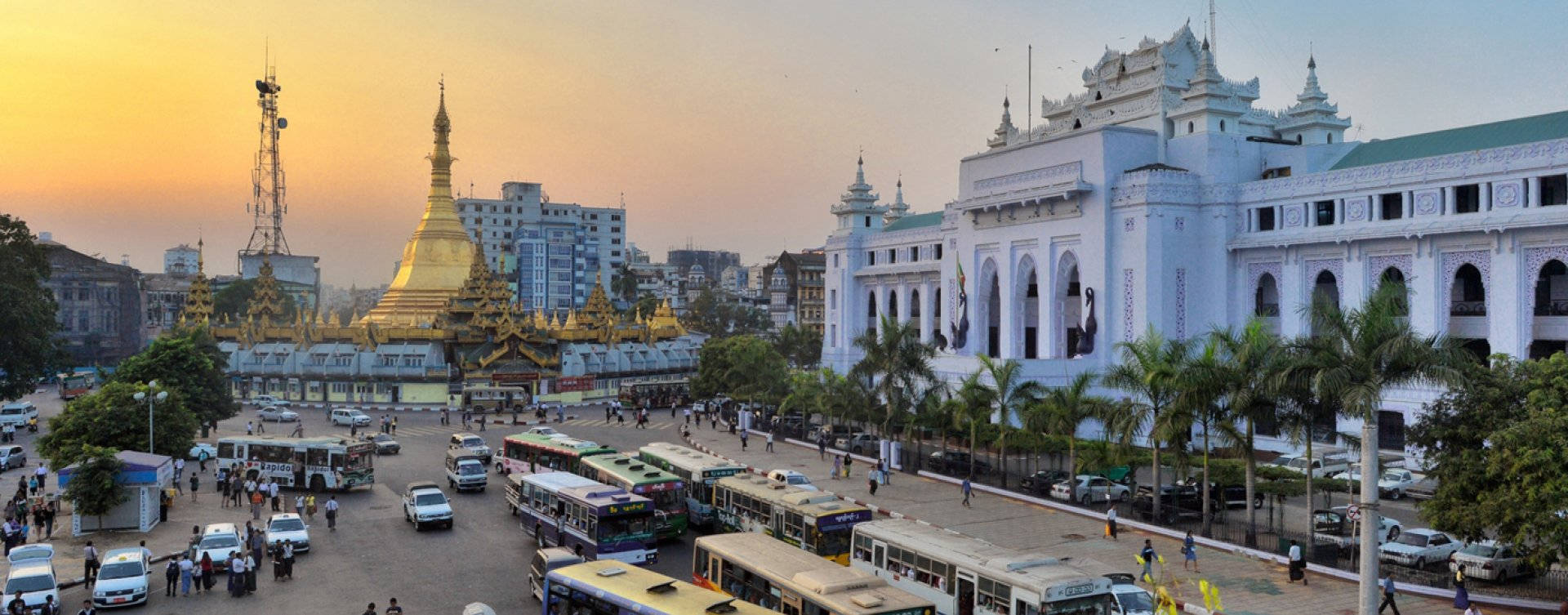 Yangon 桌布 壁紙 — 金色寶塔和白色殖民建築在日落時分閃耀，巴士和汽車擠滿了繁忙的城市廣場。