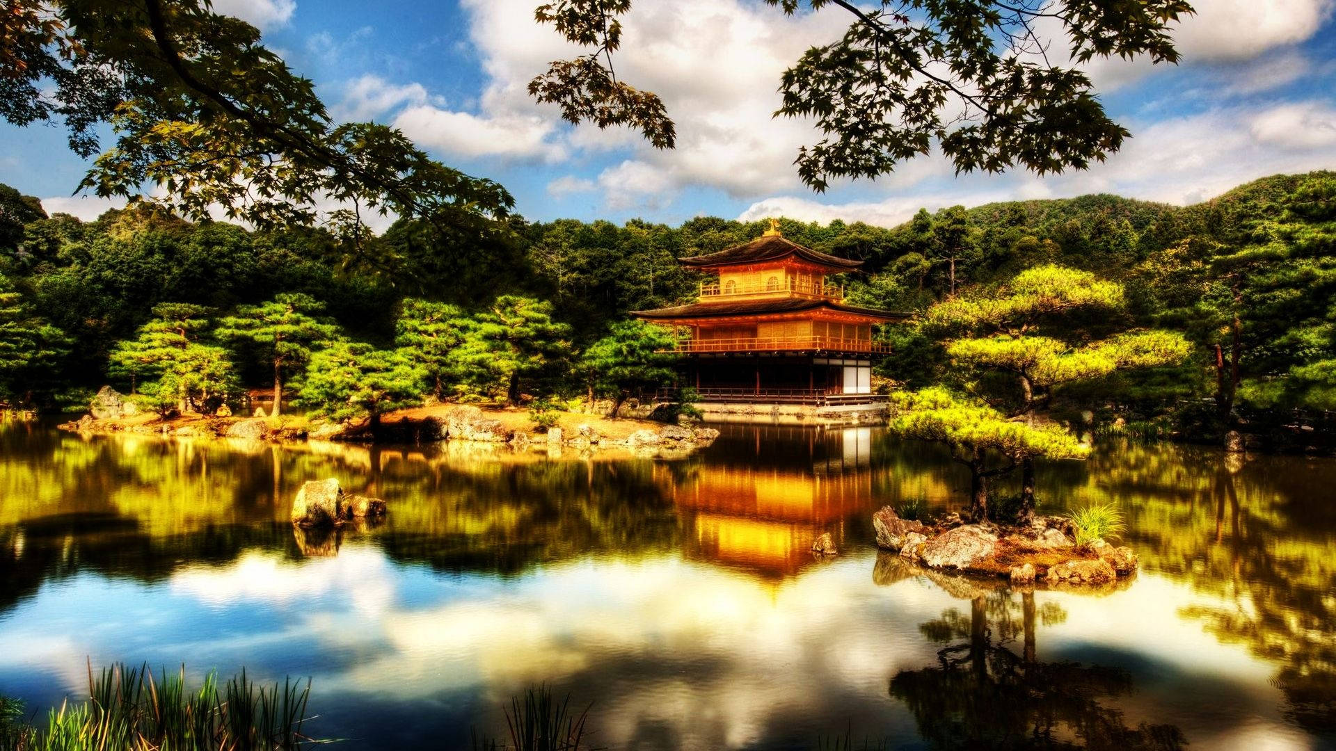 日式 桌布 壁紙 — 金色寺廟亭閣倒映在平靜的水面上，周圍是茂密的綠樹，頭頂是明亮的藍天。