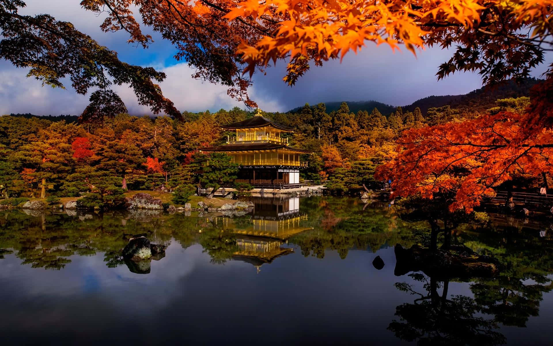 日式 桌布 壁紙 — 金色寺廟倒映在平靜的水面上，被火紅的秋葉環繞，天空壯麗。