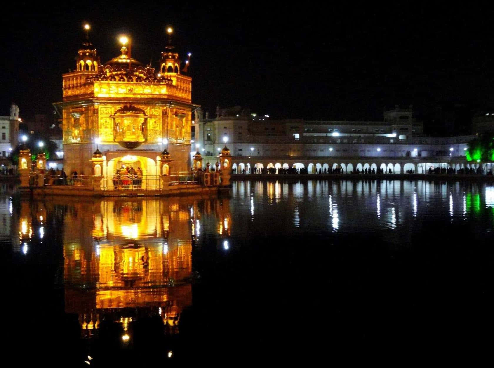 Golden Temple 桌布 壁紙 — 金色寺廟在夜晚亮燈，平靜水面上完美倒影，周圍有遊客。