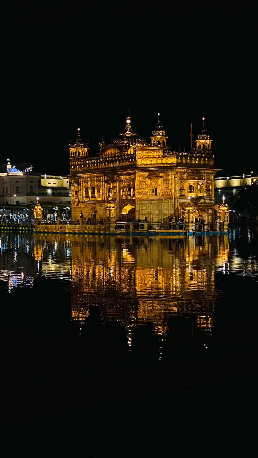 Golden Temple 桌布 壁紙 — 金色寺廟在夜晚亮起燈光，在黑暗天空下的平靜水面上完美倒映。