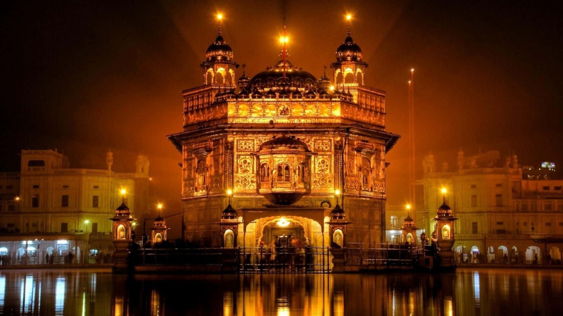Golden Temple 桌布 壁紙 — 金色寺廟在夜晚被溫暖燈光照亮，燈光在朦朧天空下倒映在周圍的水中。