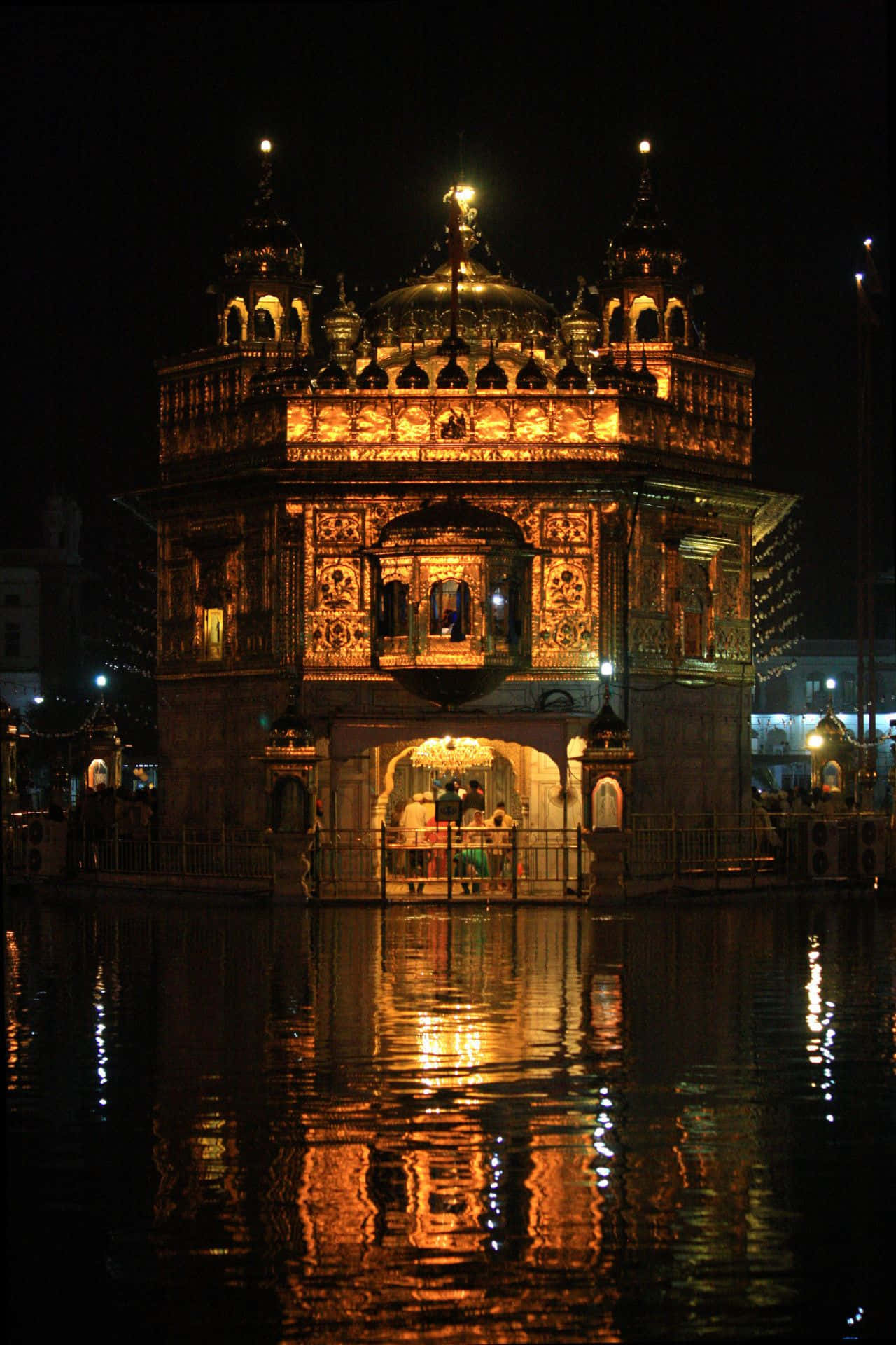 Golden Temple 桌布 壁紙 — 金色寺廟在夜晚被溫暖的燈光照亮，倒映在周圍的水中。