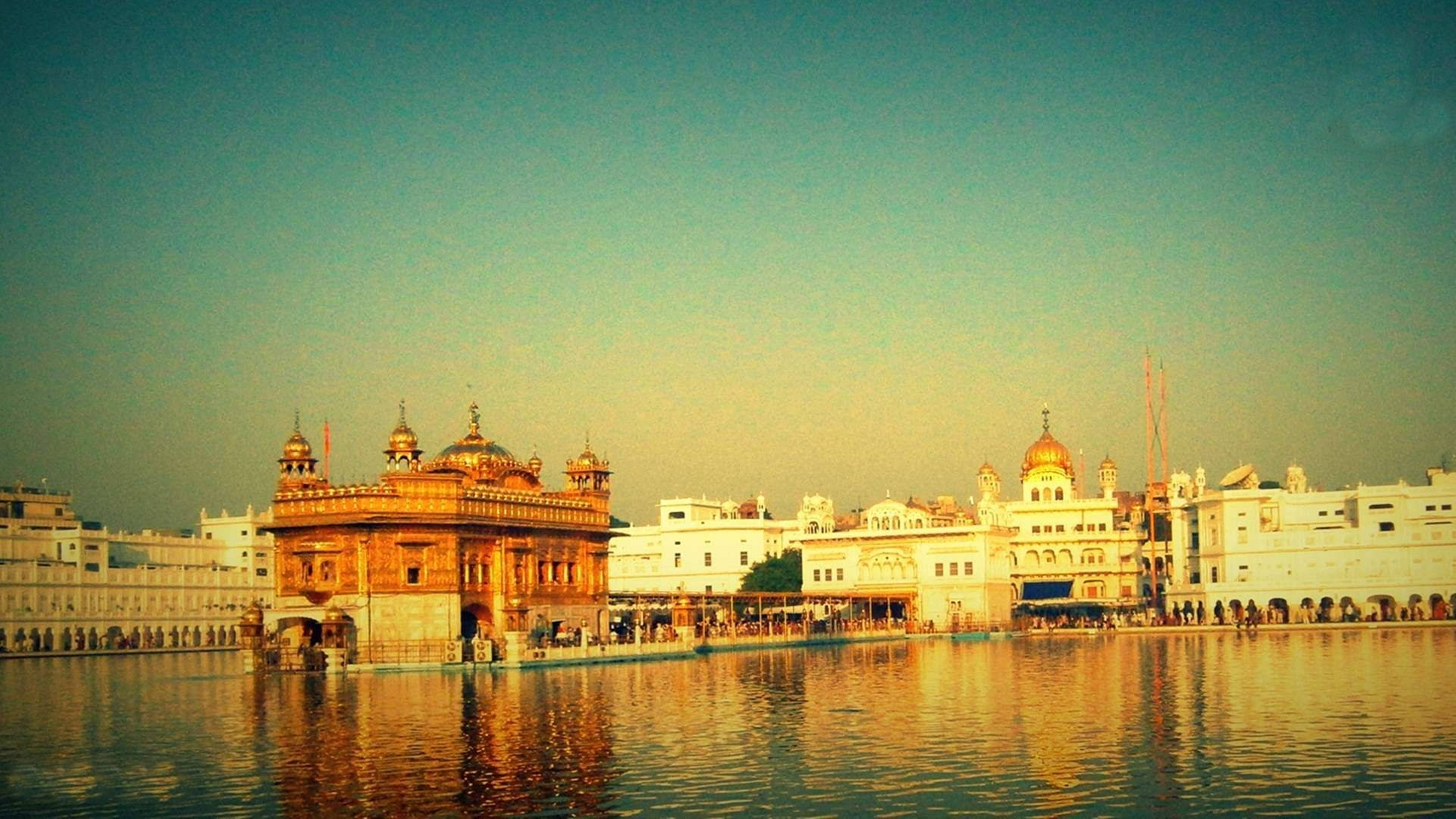 Indian 桌布 壁紙 — 金色寺廟在平靜的水面上溫暖地倒映，柔和的金色夕陽天空下。