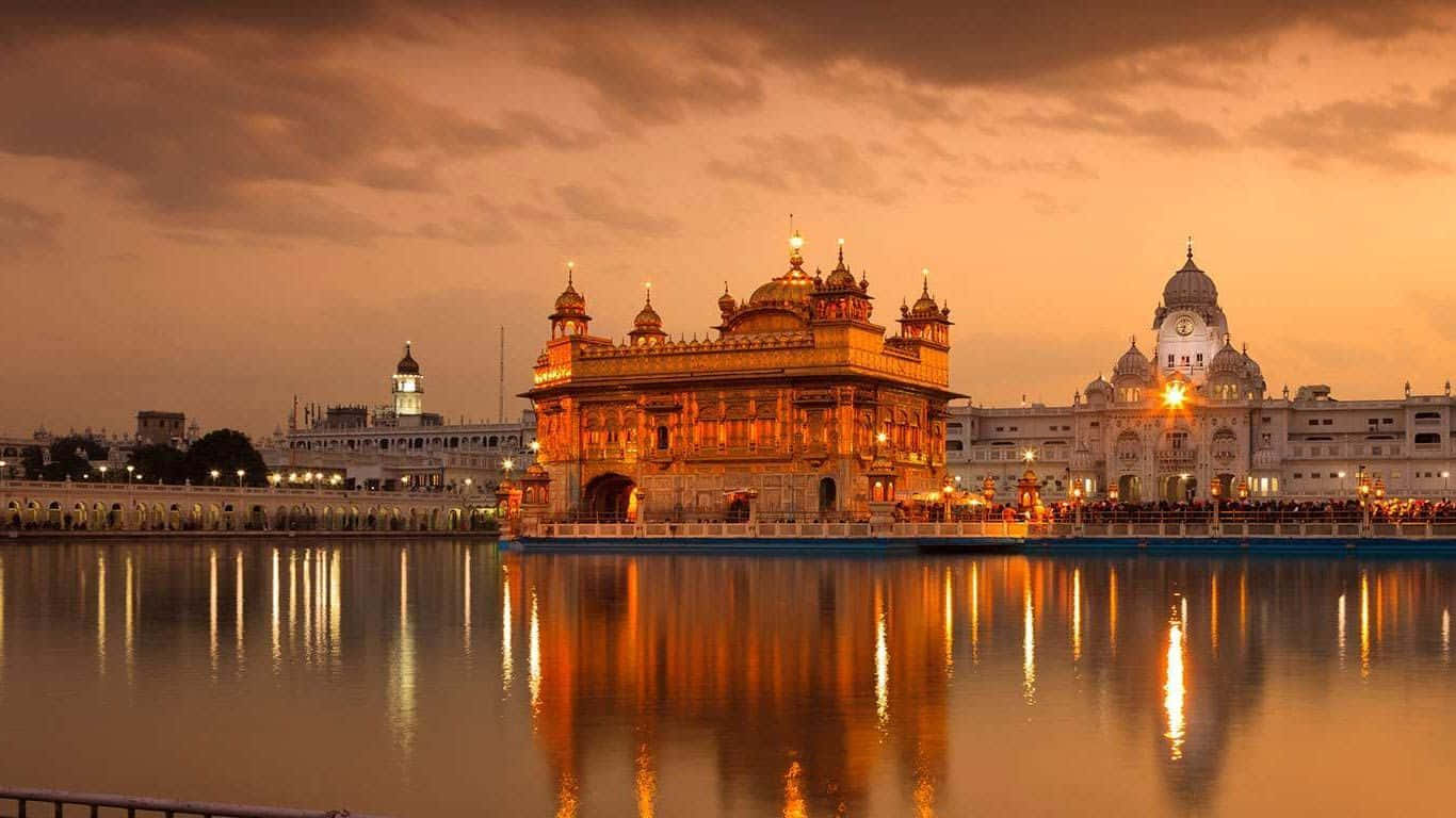 Golden Temple 桌布 壁紙 — 金色寺廟在日落時被照亮，溫暖的倒影在平靜的聖池上閃爍。